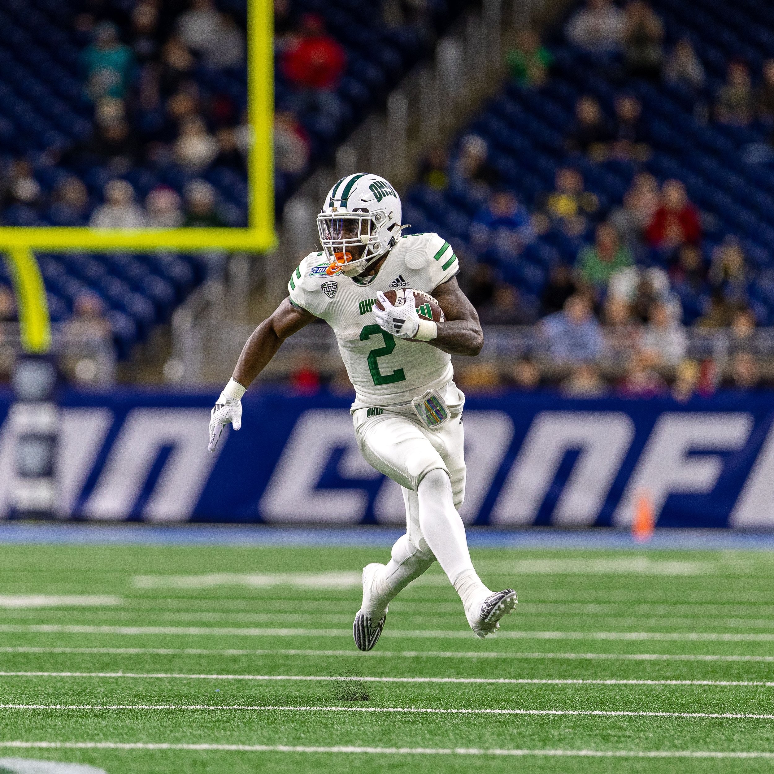 A football player wearing a white uniform with green accents, number 2, running on the field with a football in his hand, during a game.