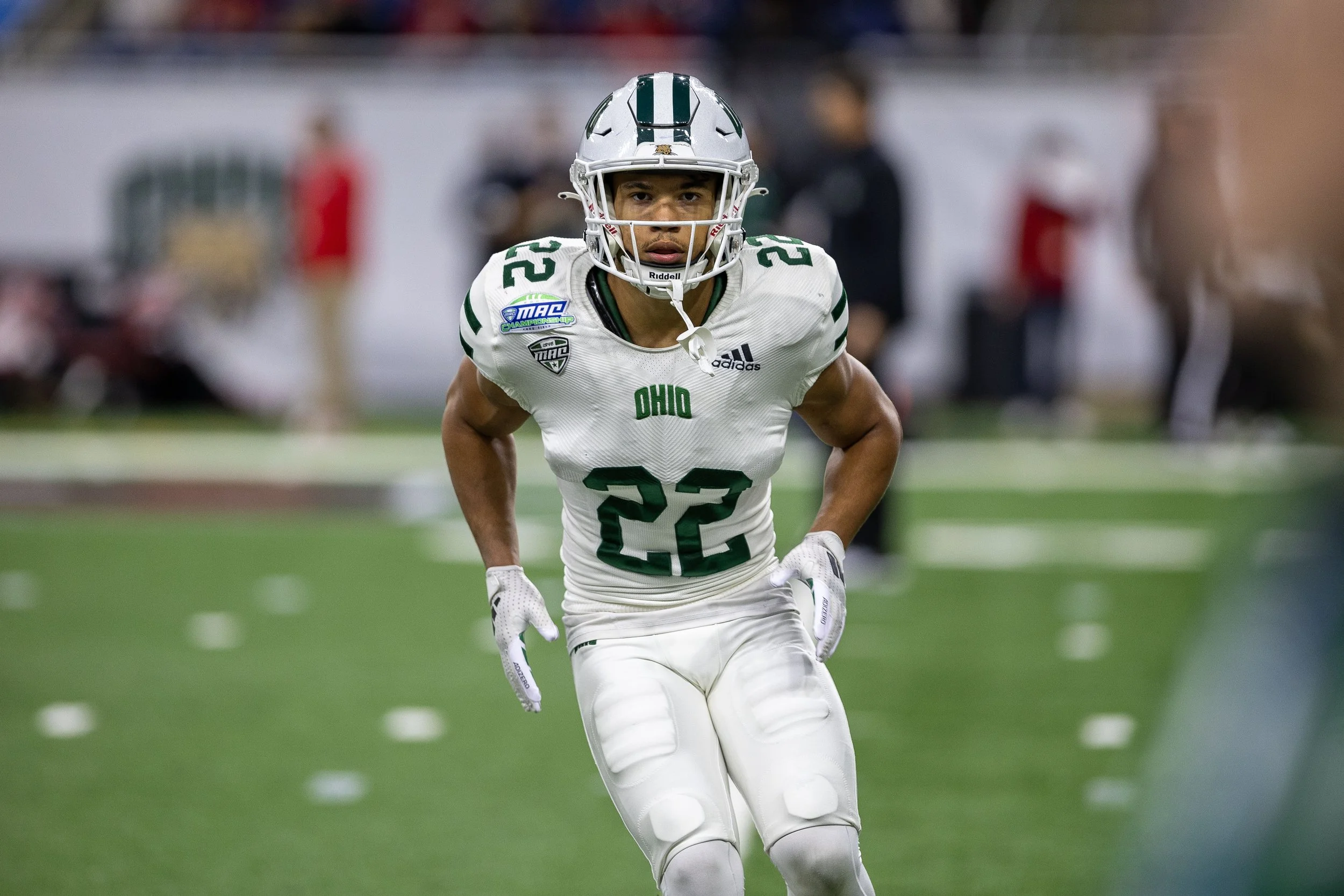 An Ohio State football player wearing a white uniform with green accents, number 22, in a ready stance on the field during a game.