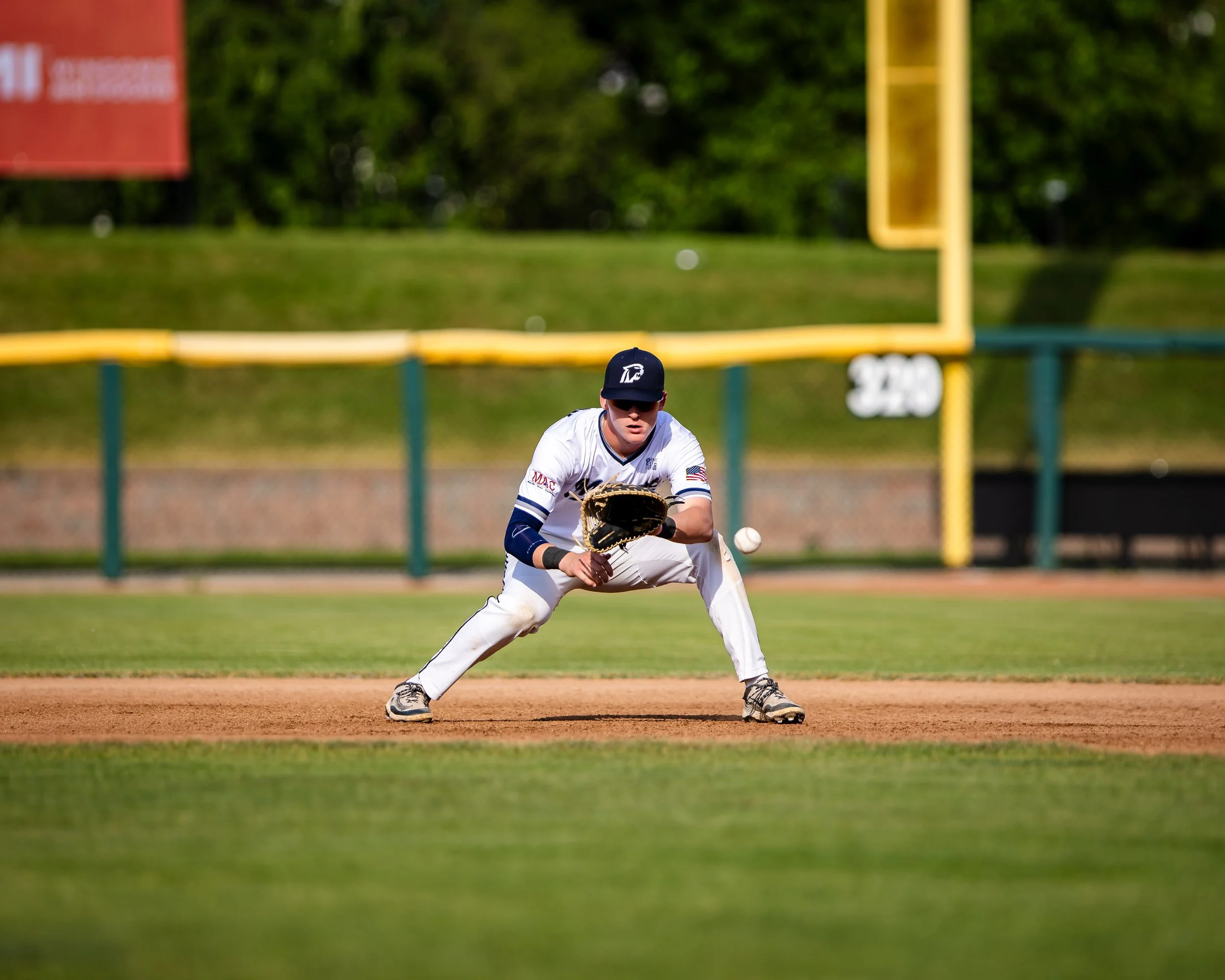 A baseball player in a white uniform and black cap fielding a baseball on the infield during a game.