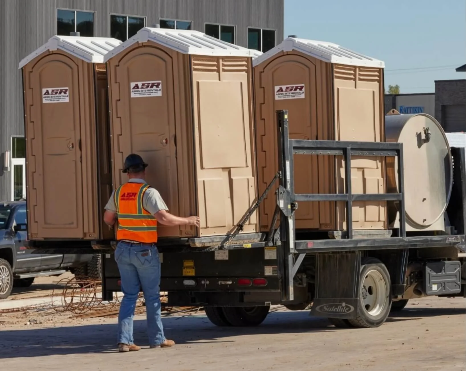 Worker in an orange safety vest beside portable toilets loaded on a flatbed truck