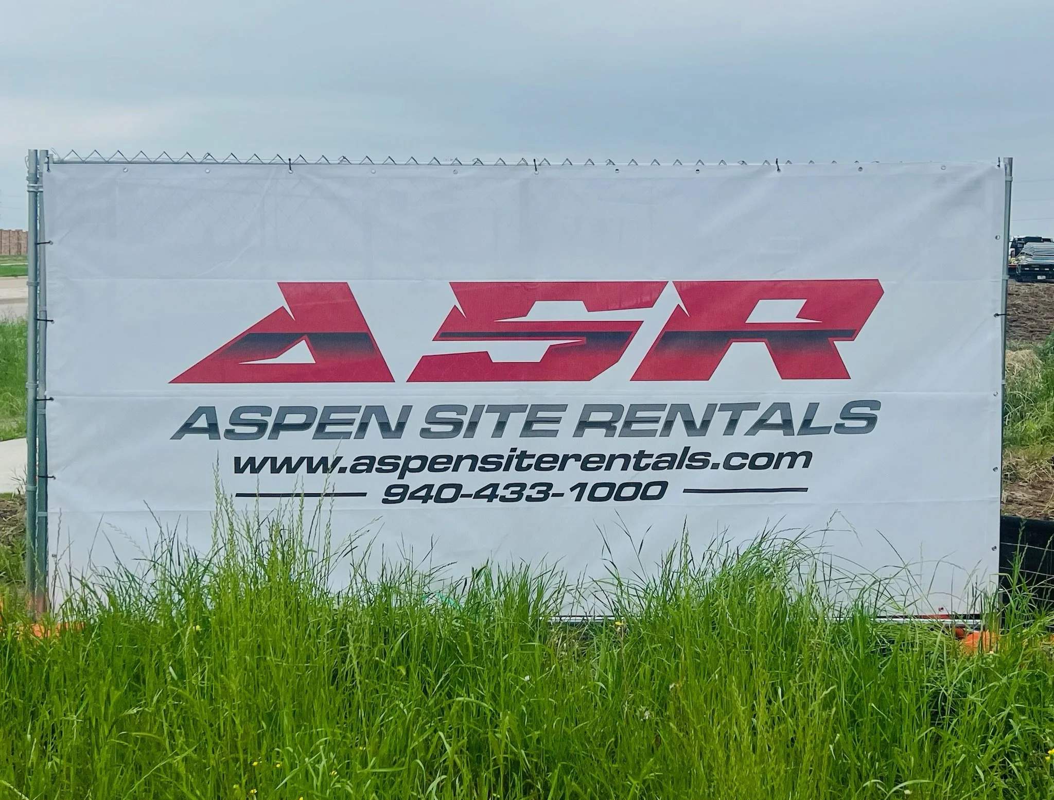 Printed Aspen Site Rentals banner screen zip-tied to a fence with web address and phone