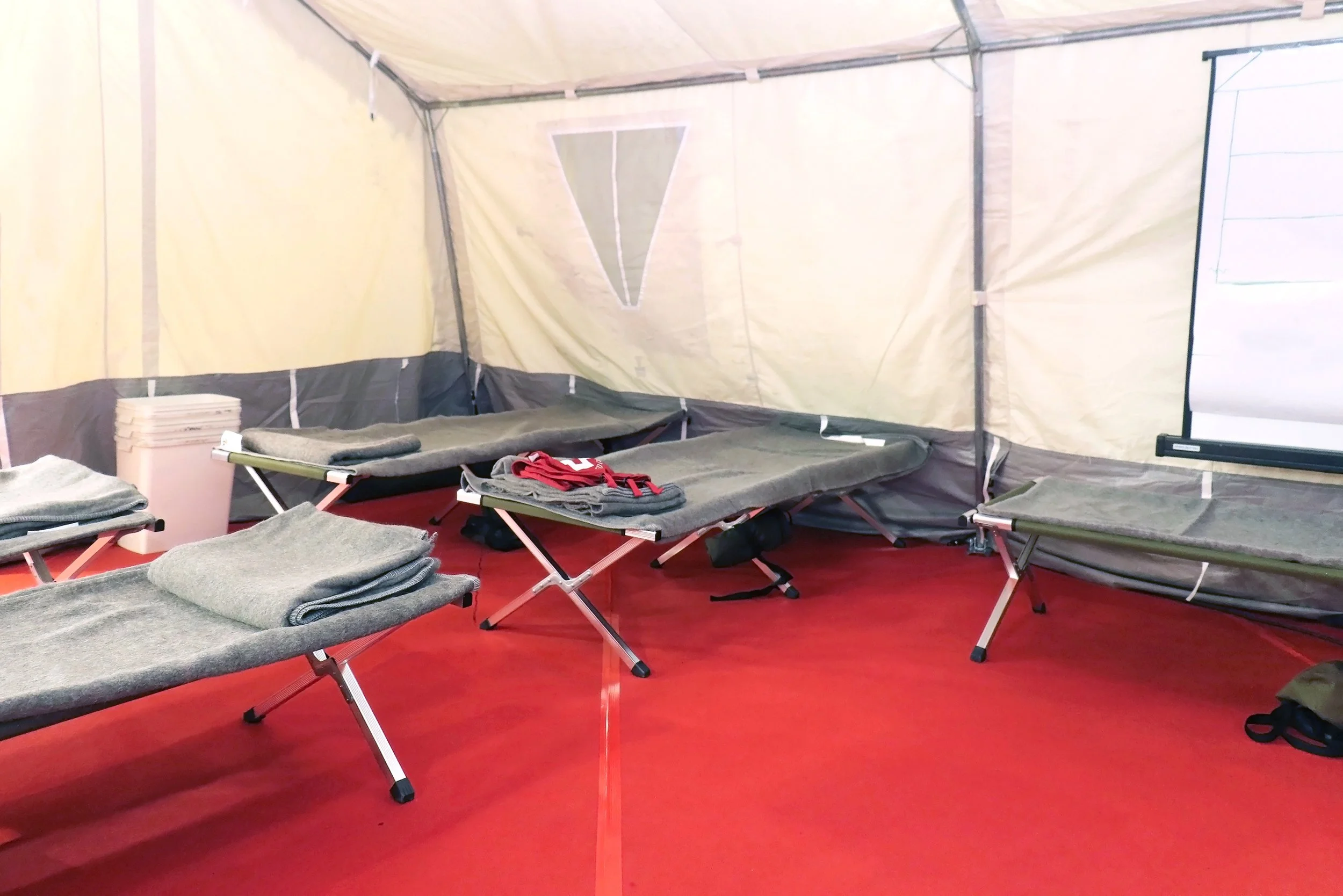 Folding cots with gray blankets inside a white tent