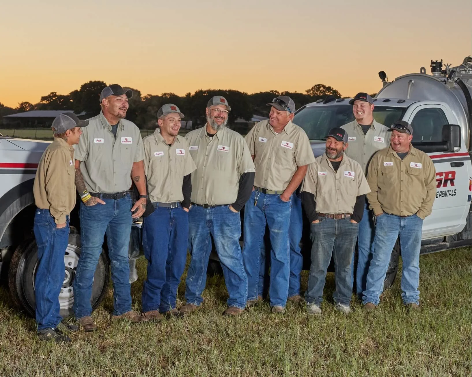 Aspen Site Rentals crew in uniform standing by company trucks at sunset