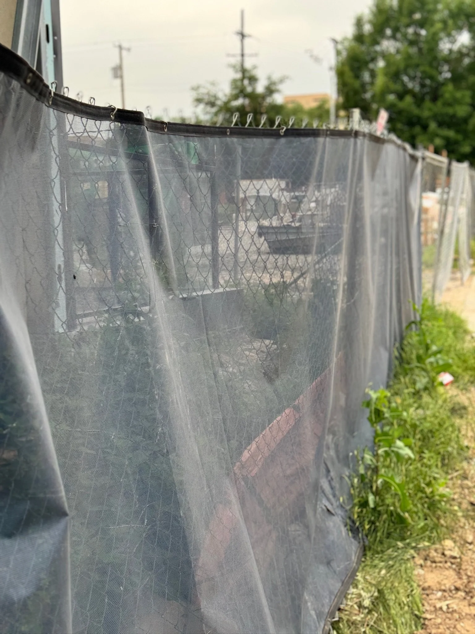 Dark mesh windscreen on a chain-link fence along a dirt path