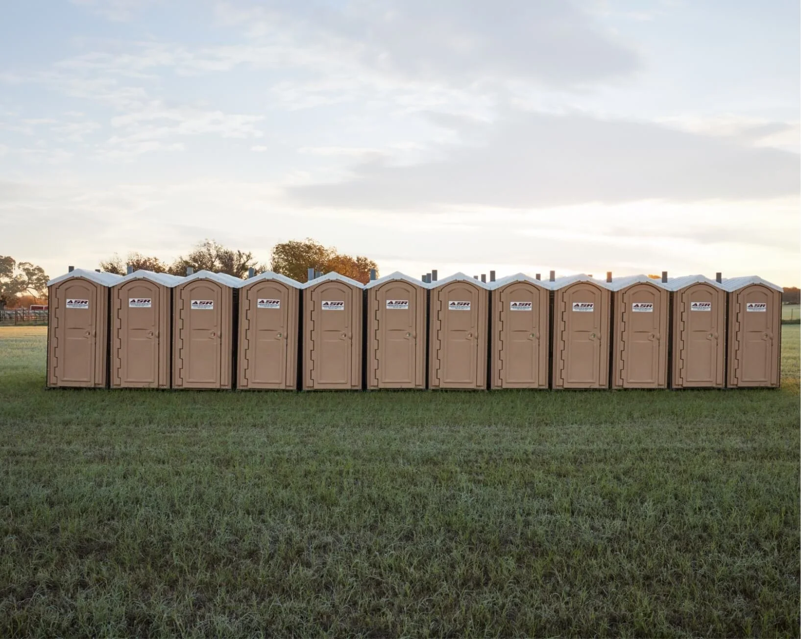 Row of portable toilets set up in an open field at dusk
