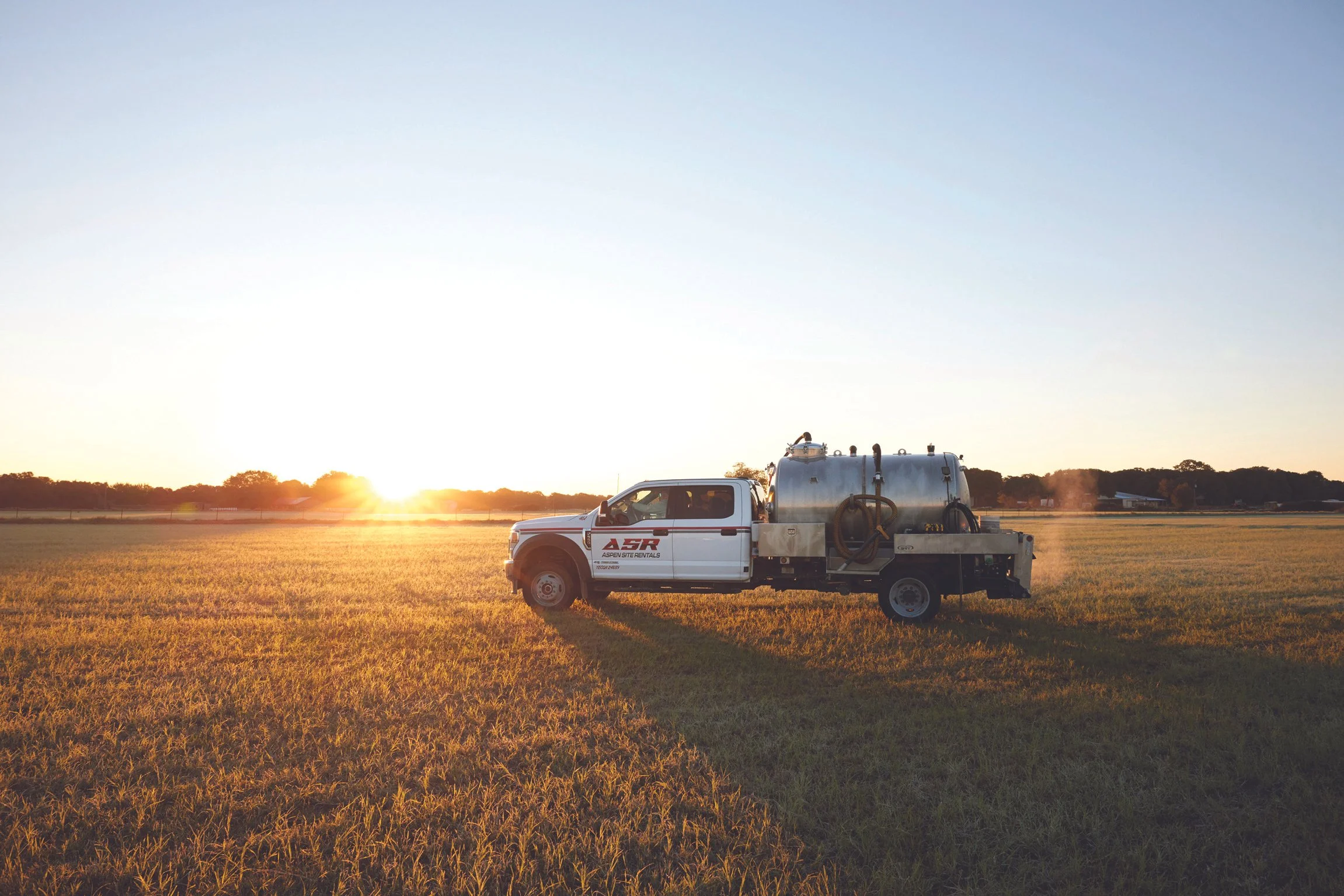 Aspen Site Rentals service truck with a pump tank in a field at sunset