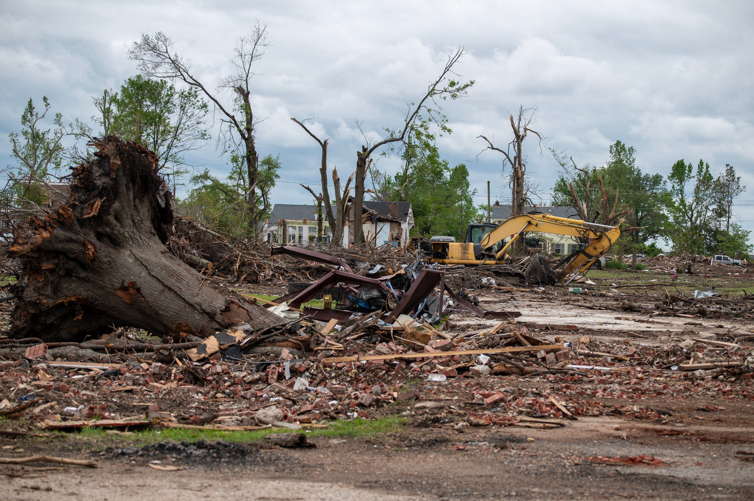 Storm debris and an uprooted tree with an excavator behind
