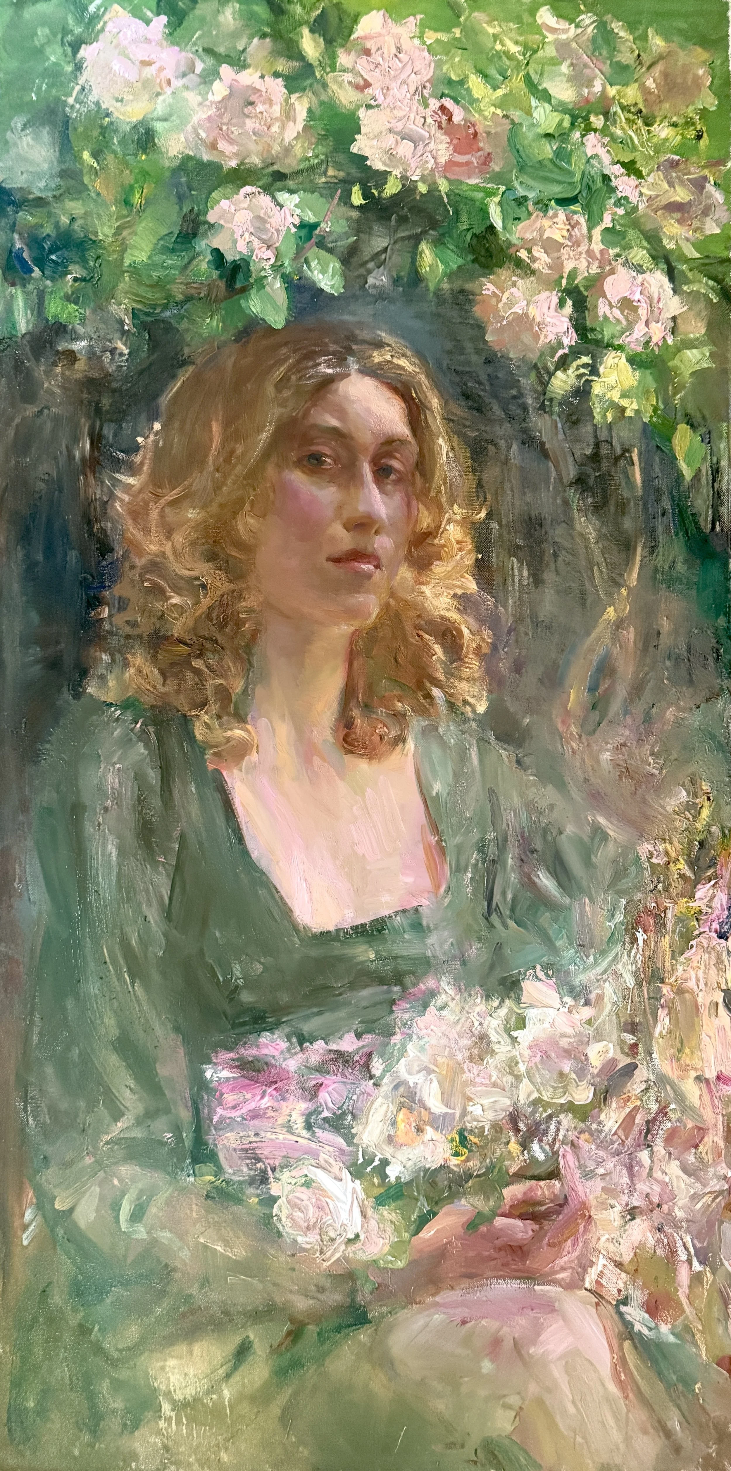 Oil painting of a woman with curly, light brown hair, wearing a dark green dress, sitting among pink and white flowers with green foliage in the background.