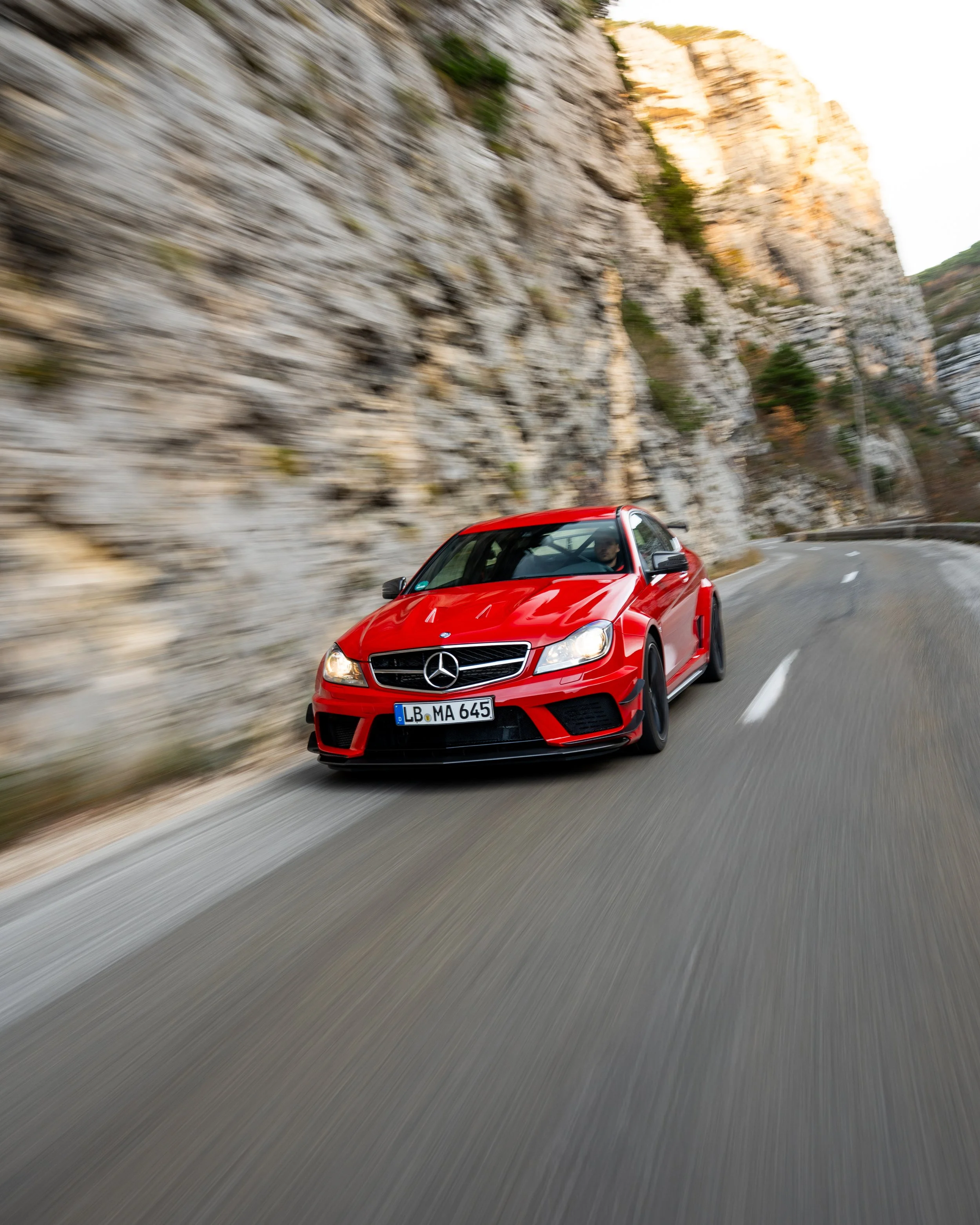 Ein rotes Mercedes-Auto fährt auf einer kurvigen Bergstraße entlang einer steilen Felswand.