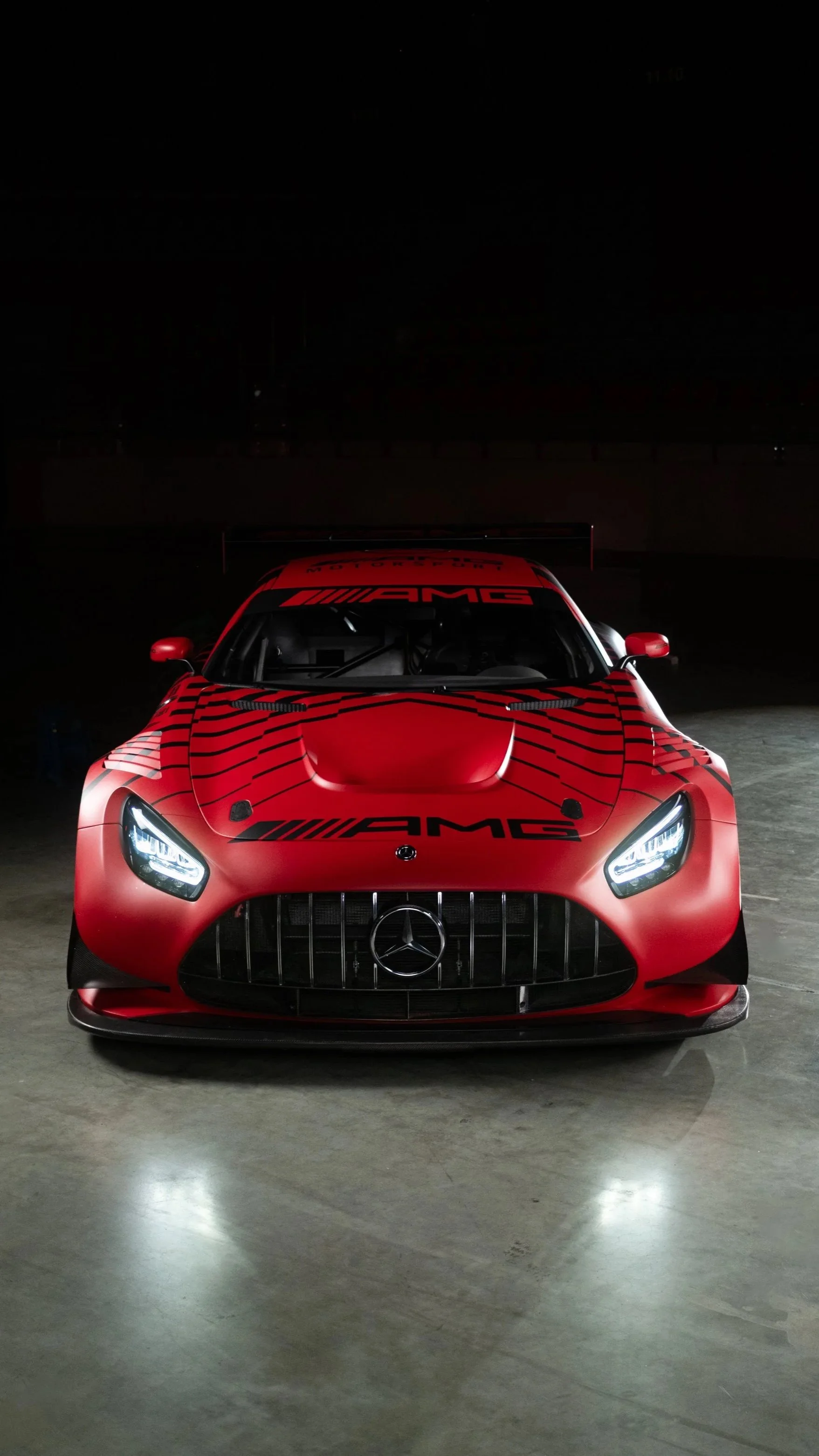 Ein rotes Mercedes-AMG Supersportwagen mit AMG-Logo auf der Haube, bei Nacht, im Dunkeln.
