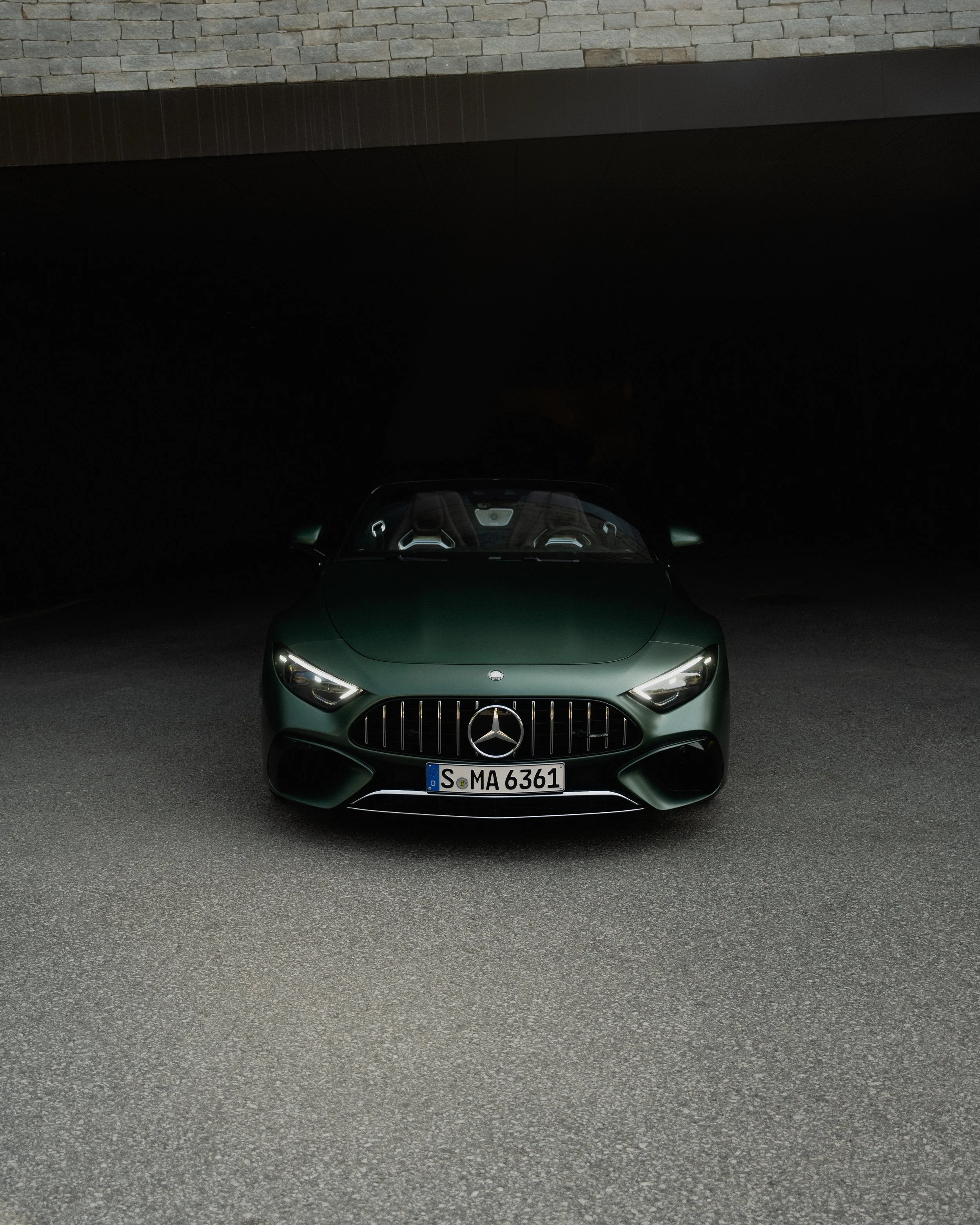 Ein grüner Mercedes-Benz Sportwagen steht auf einer dunklen Straße vor einer Wand mit Ziegelmauer.