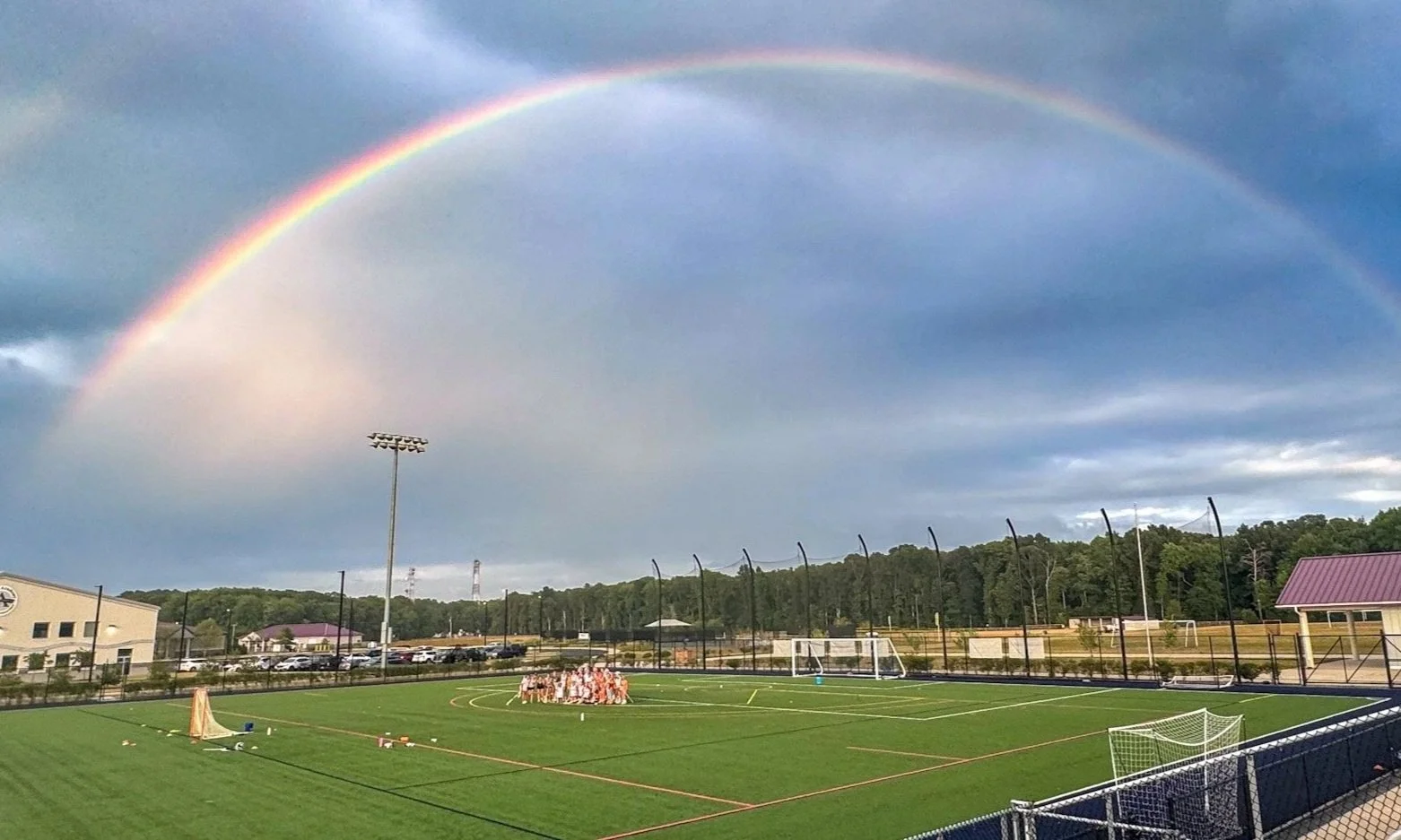 A rainbow over a sports field with a group of players, likely a soccer team, gathered in the center.