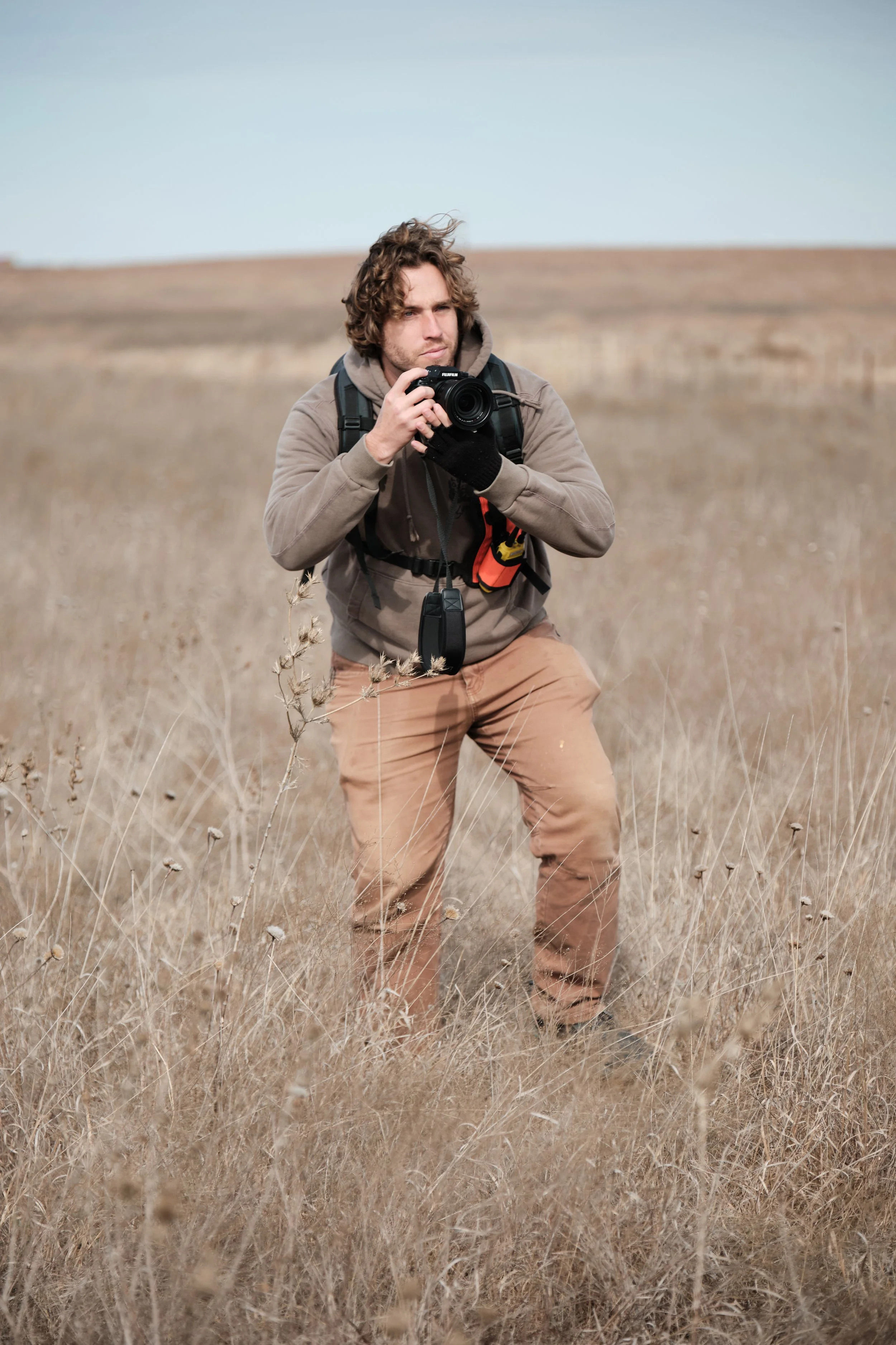 Charles taking a photo with a camera in a dry grass field