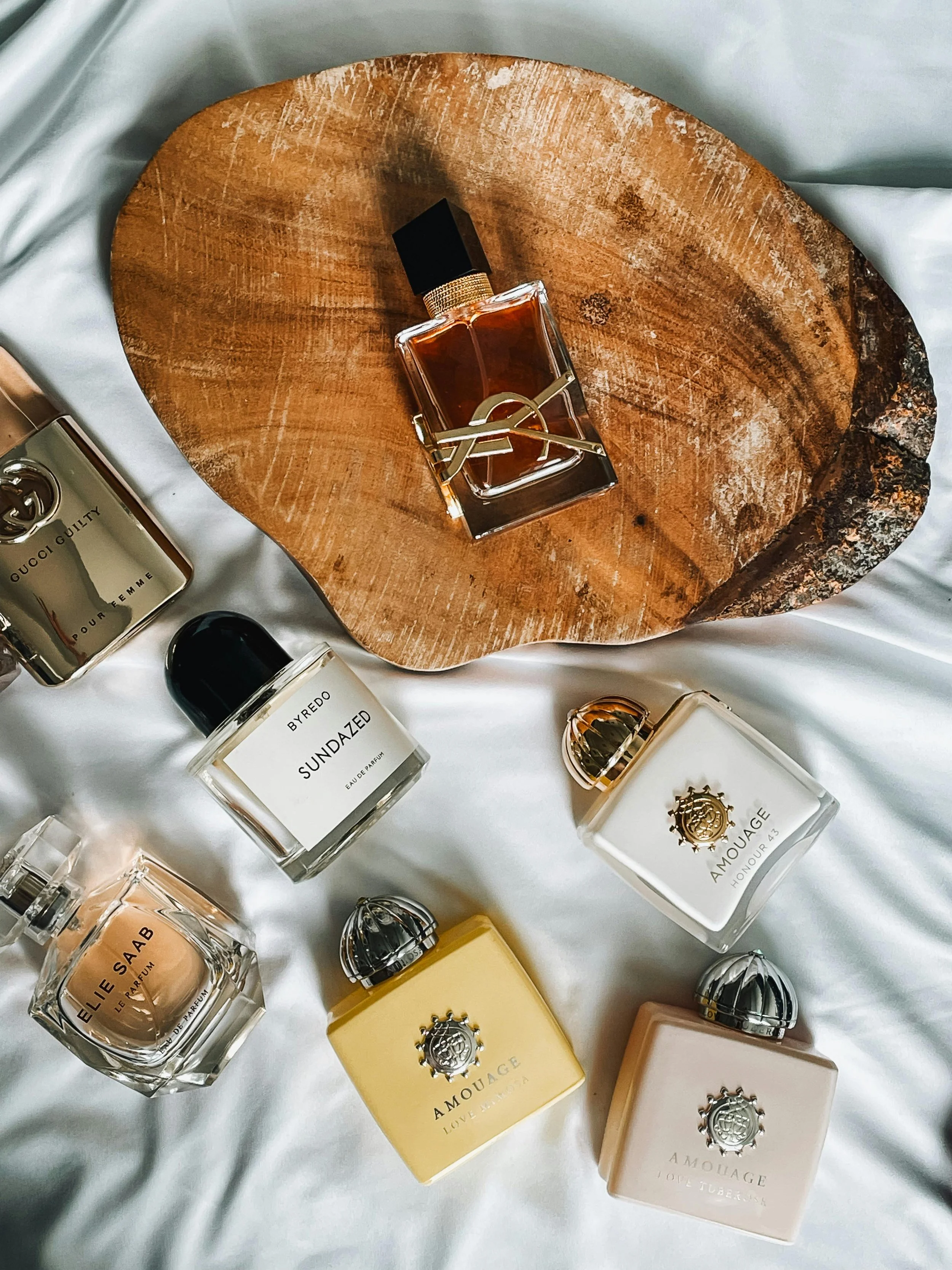 Collection of perfume bottles on white fabric and a round piece of wood.