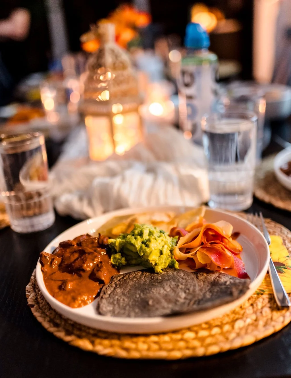 A plate of food including mashed avocado, a fish fillet, and a serving of meat and vegetables at a dinner table with drinks and candles.
