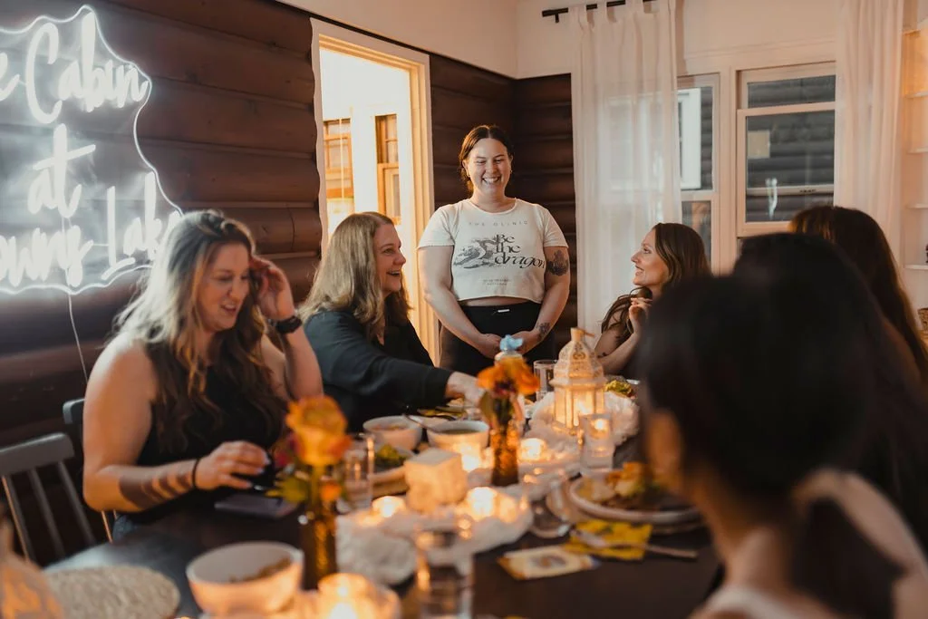 Group of women enjoying a meal at a table in a cozy, wood-paneled room with a neon sign and candles.