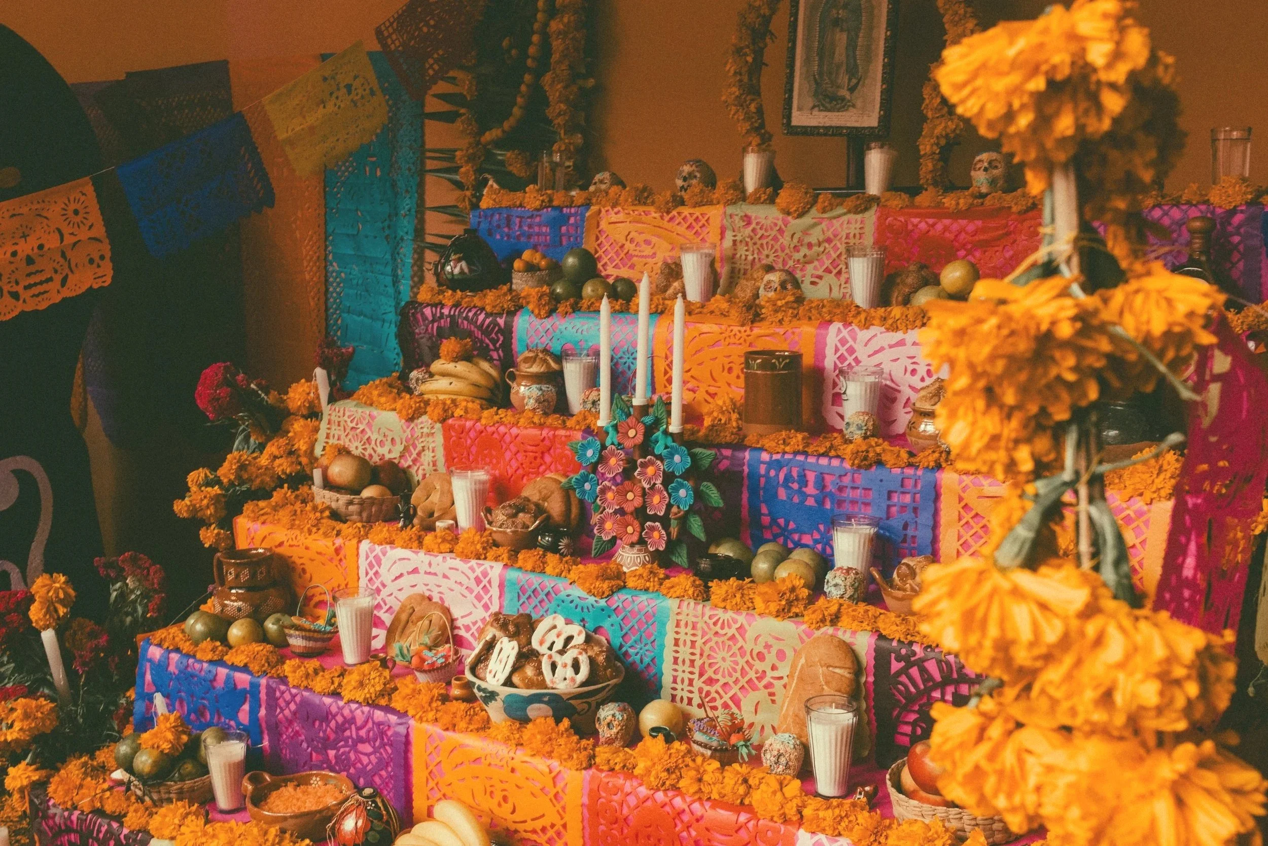 Colorful altar decorated with marigold flowers, candles, fruits, and traditional decorations for a Day of the Dead celebration.