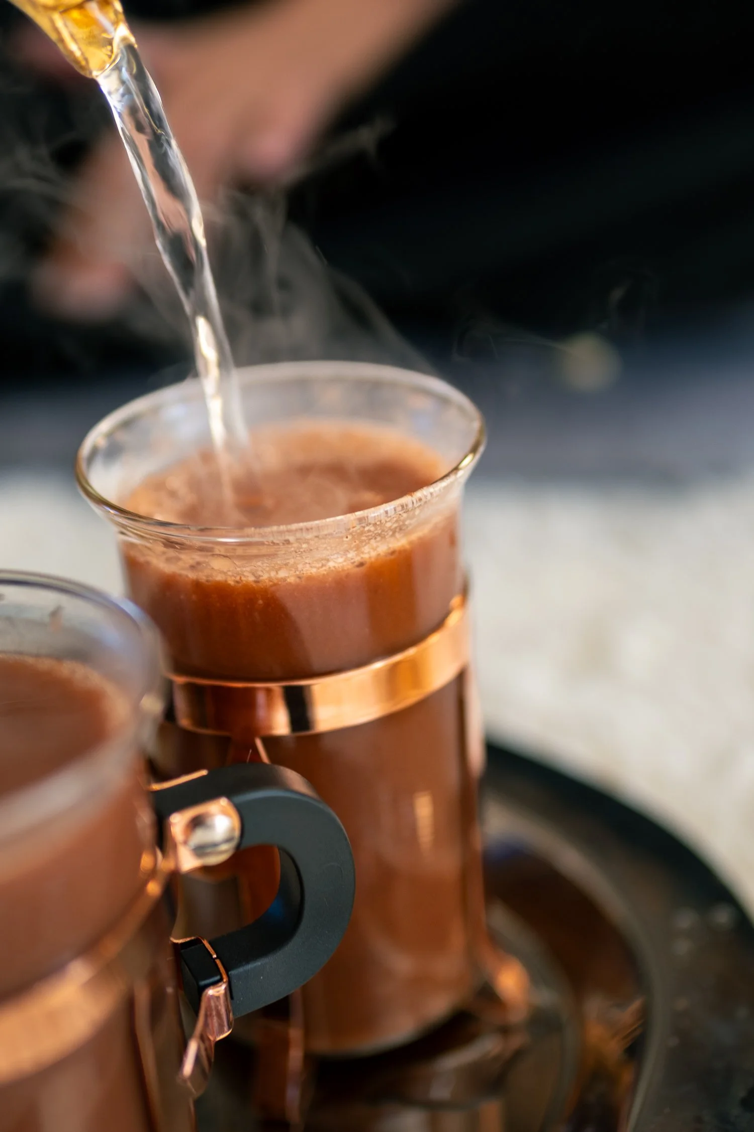 Close-up of a hand pouring hot water into a copper moka pot, used for making espresso.