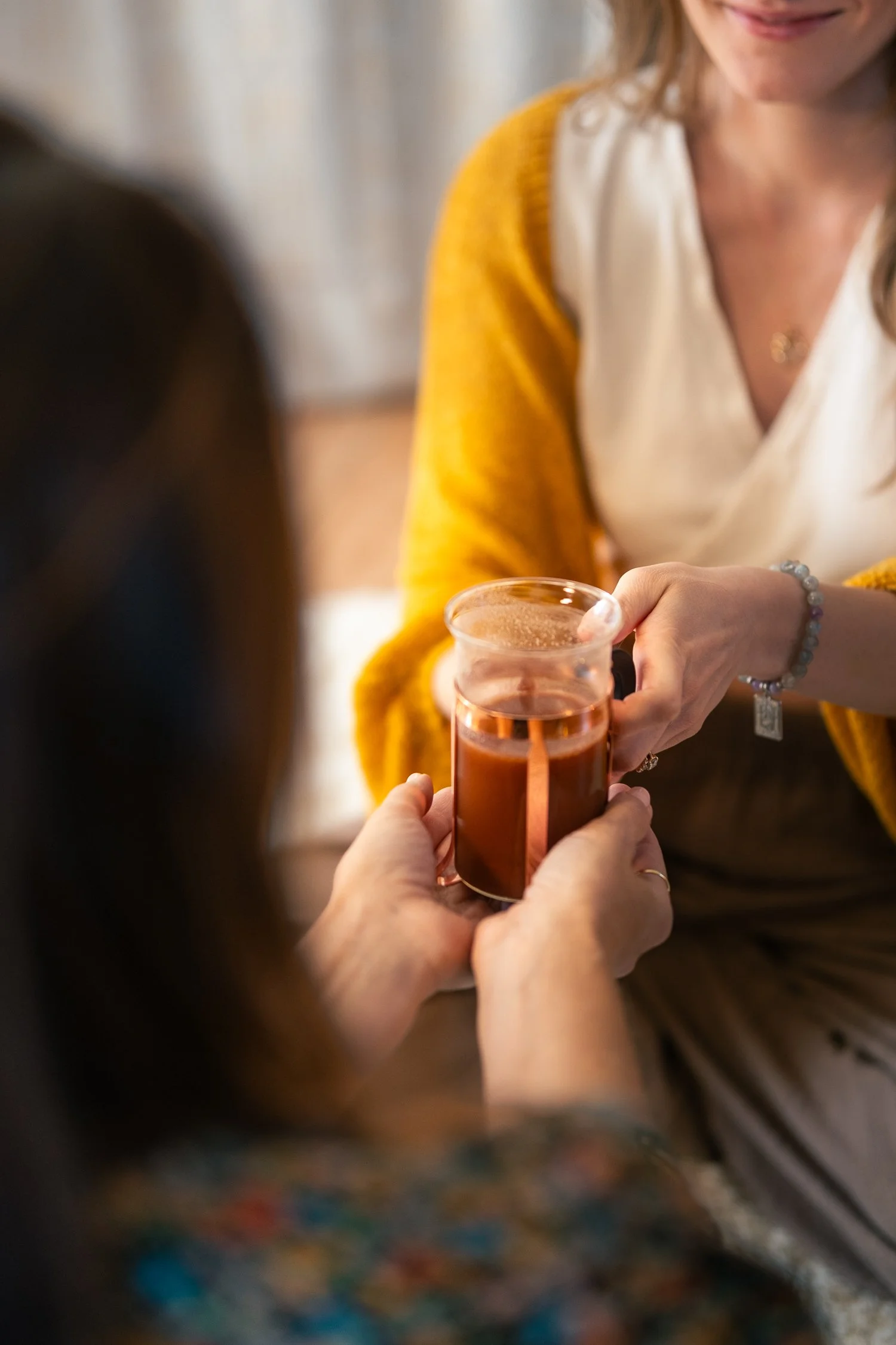 A person with a yellow sweater pouring a drink from a small bottle into a glass held by another person.