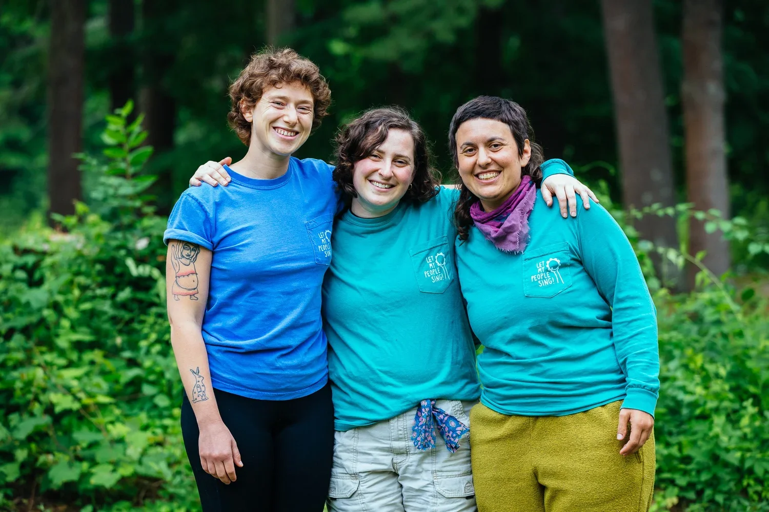 Serena, Batya, and Margot pose and smile for the camera with their arms around each other
