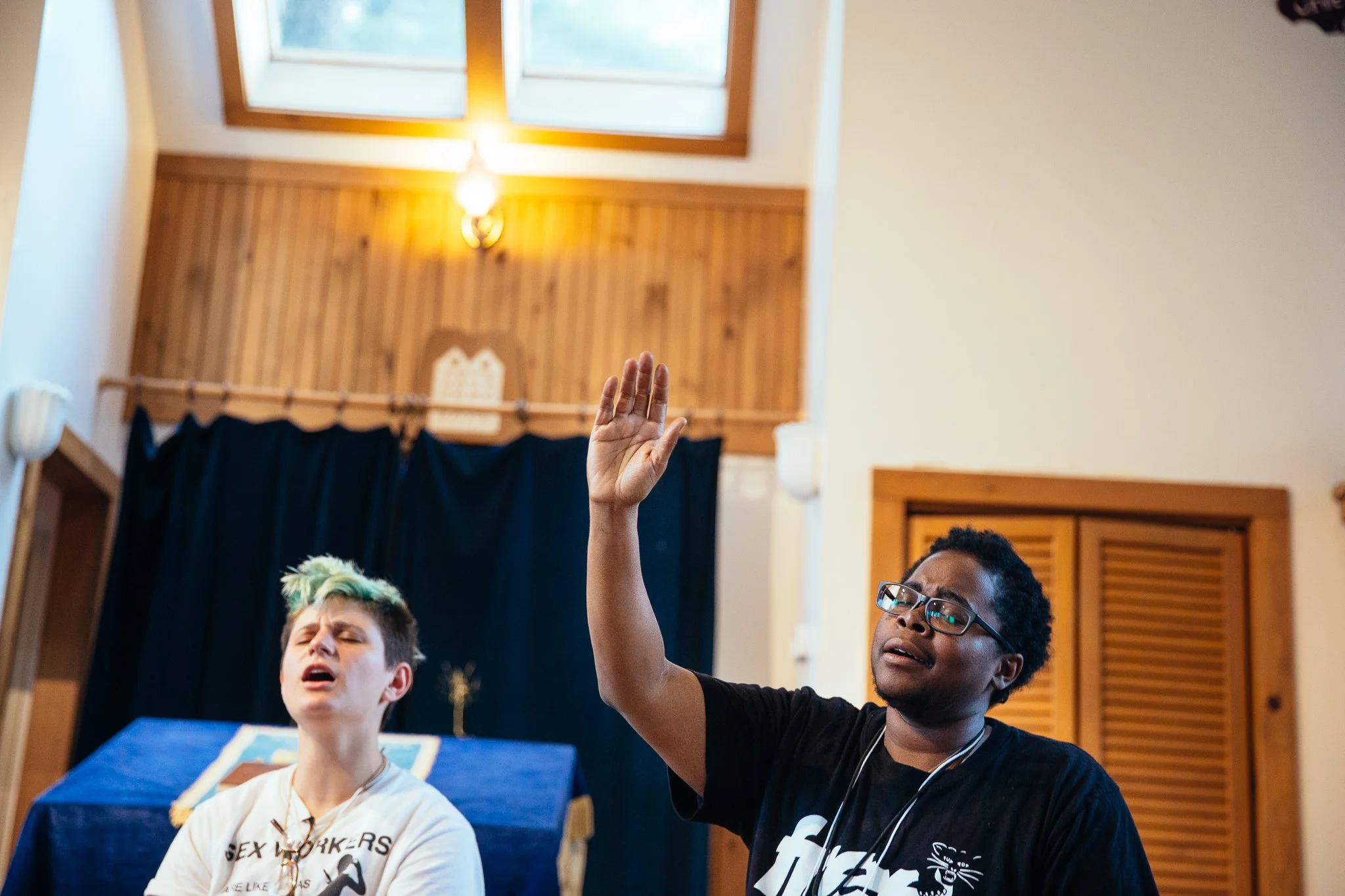 A photo of two people singing indoors, one with their hand raised in the air
