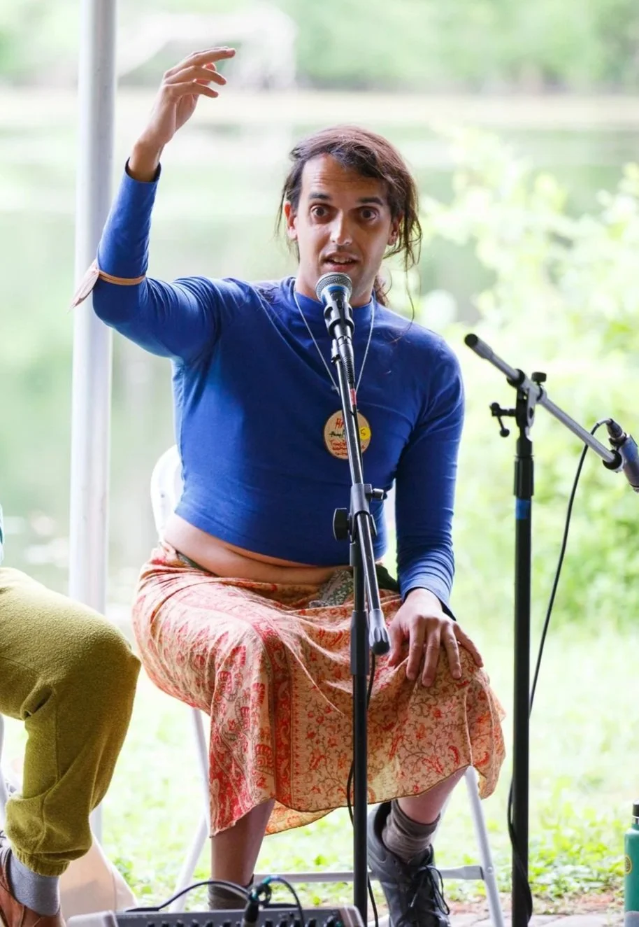 Someone sits in front of a microphone, speaking to a crowd