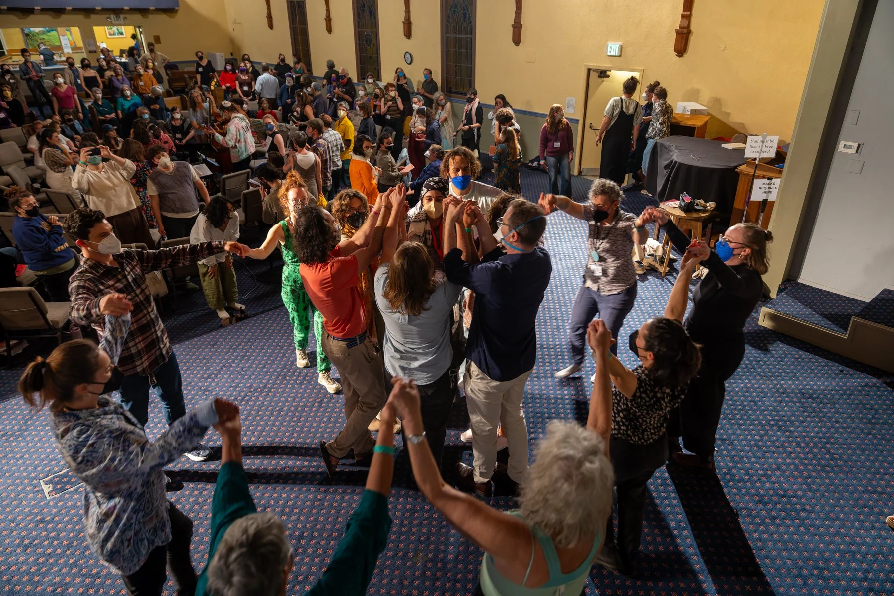 A large crowd gathered in a synagogue, with some people in the front dancing in two concentric circles