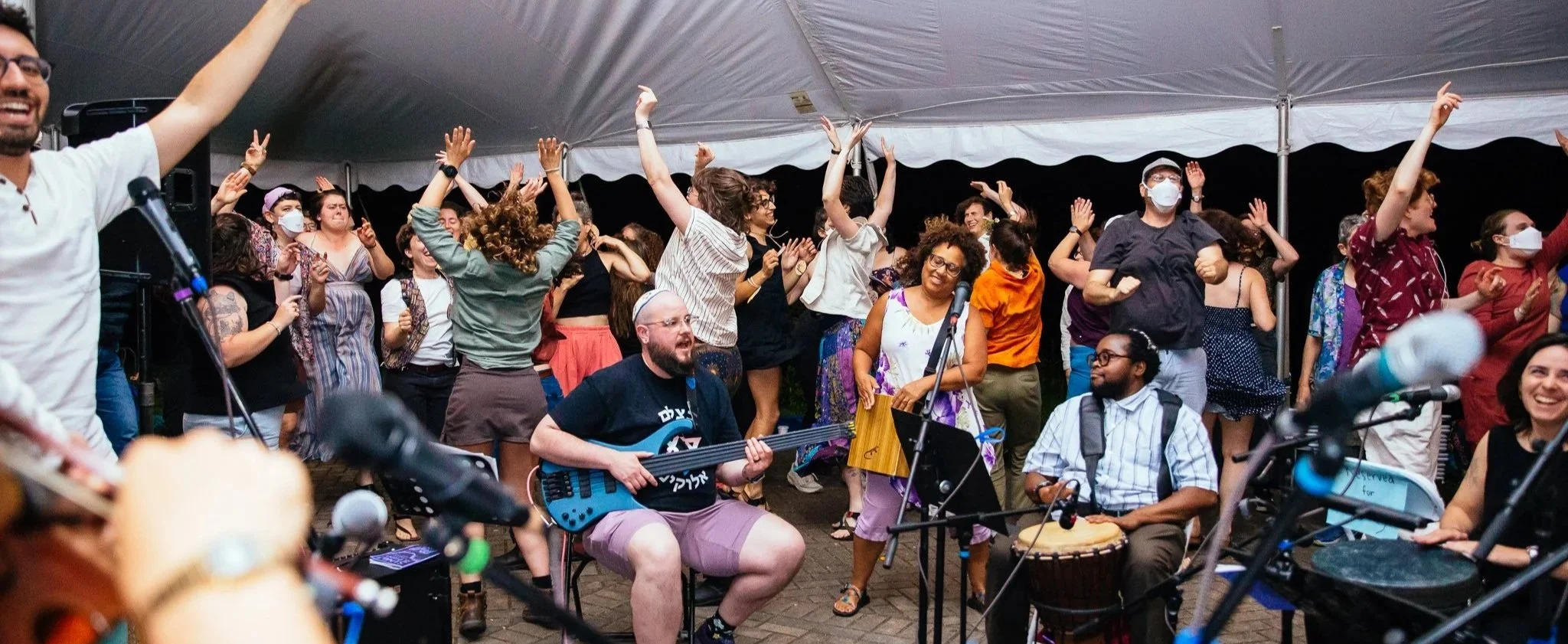 A large crowd dancing, singing, and playing instruments under a large white tent
