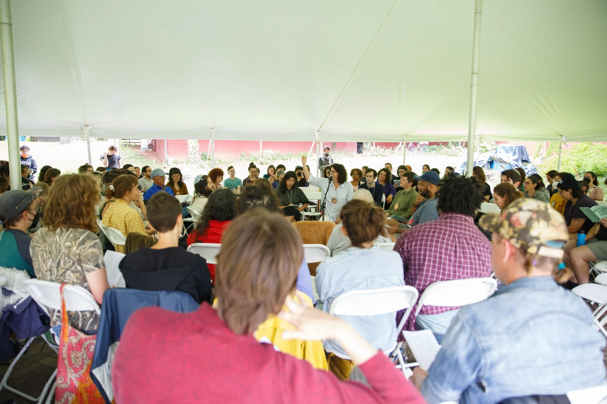 A photo of a large crowd sitting in folding chairs in concentric circles under a large white tent