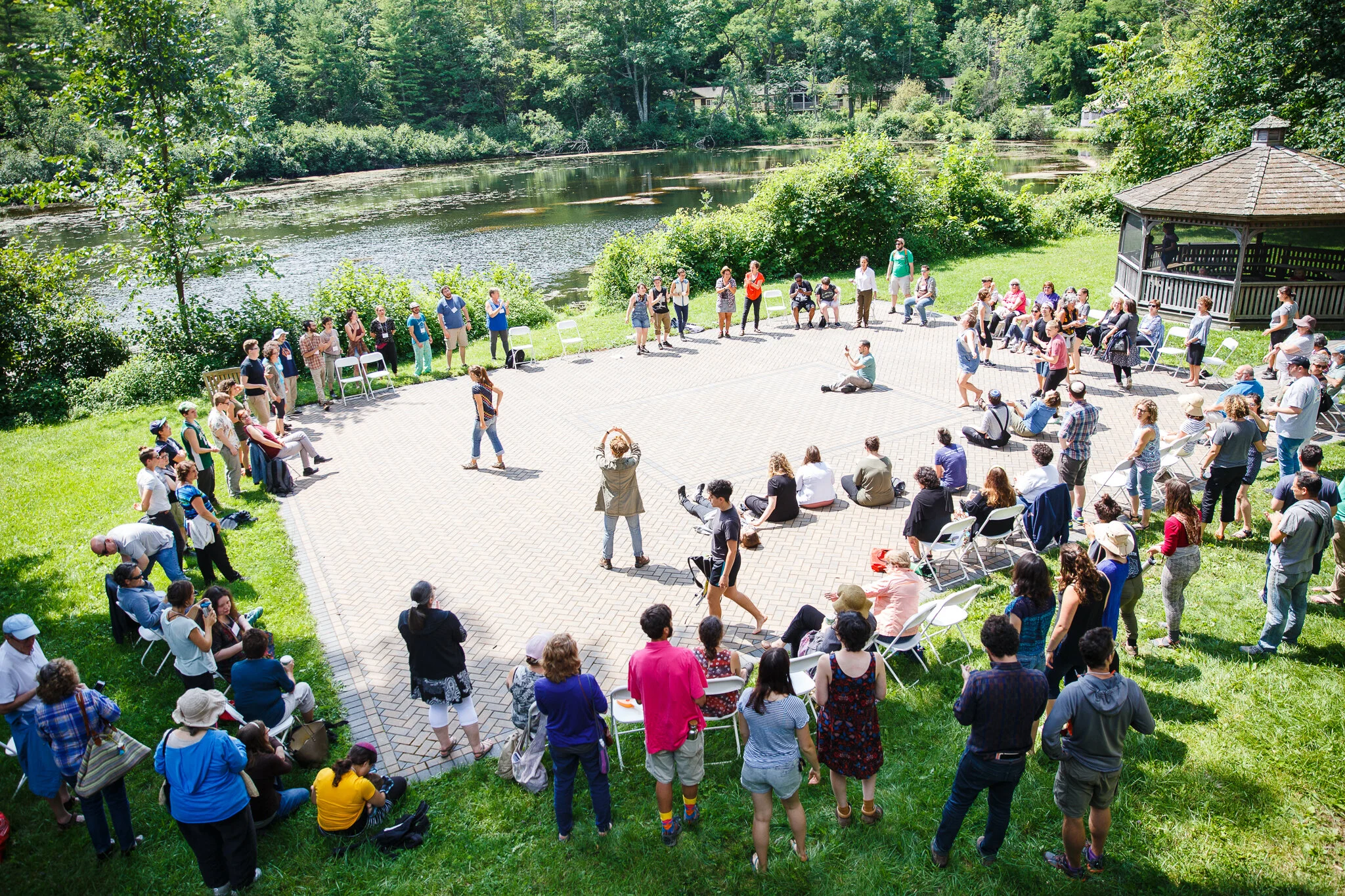 A large crowd gathers outside around a brick platform, sitting, standing, and walking around, talking to each other