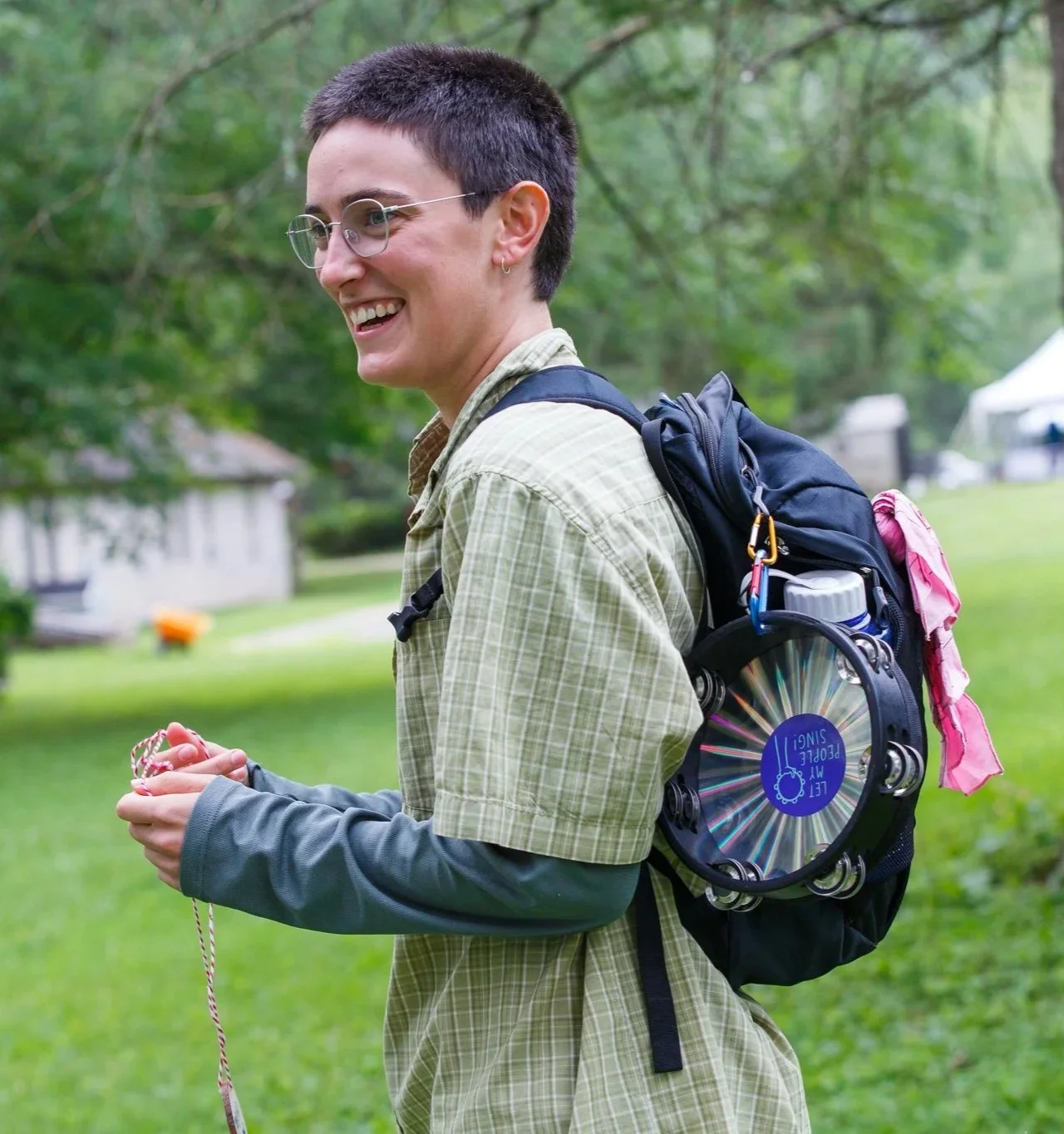 A photo of Maya at the summer retreat, wearing a backpack with a tambourine attached