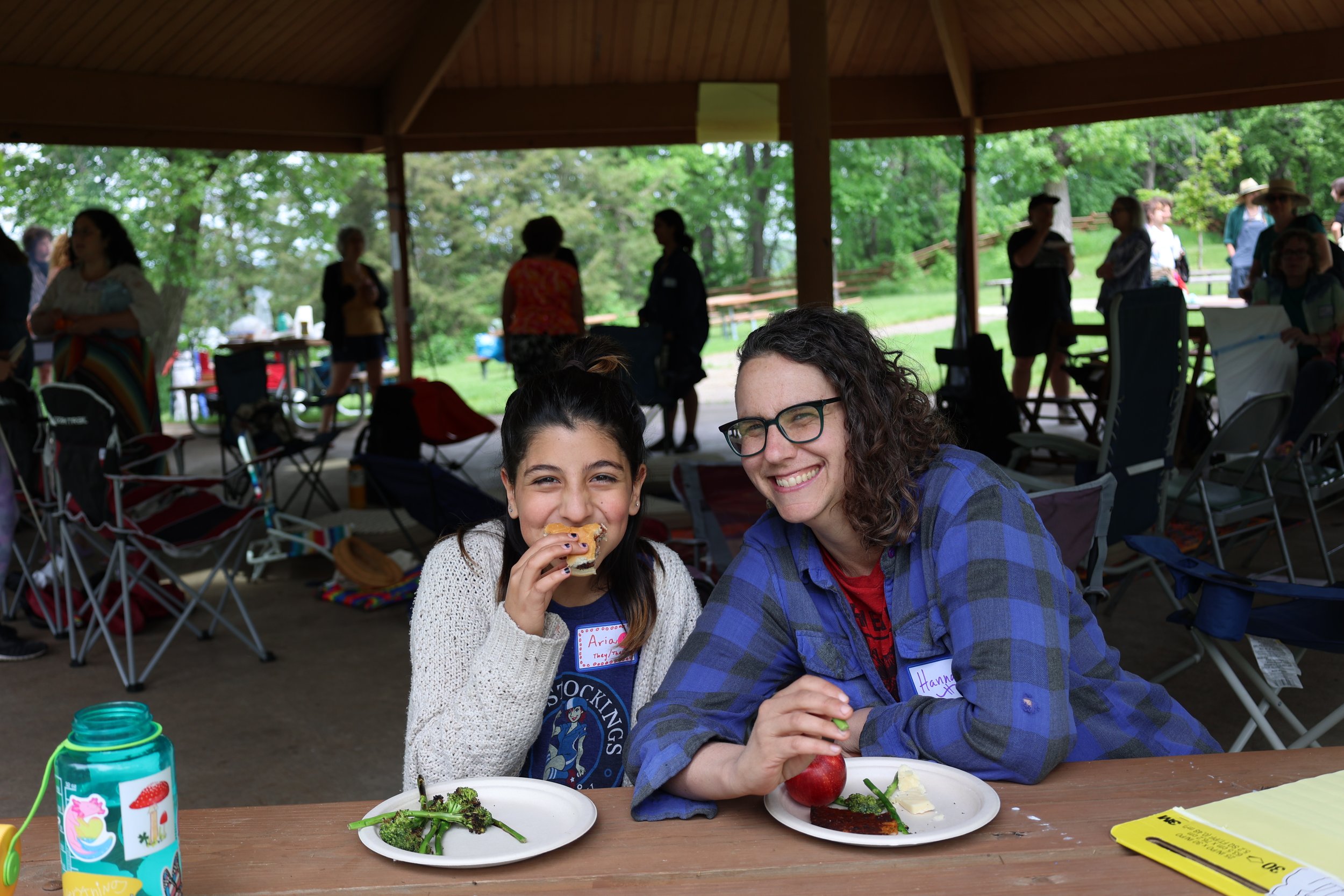An adult and a kid sit at a table with plates full of food, eating and smiling towards the camera
