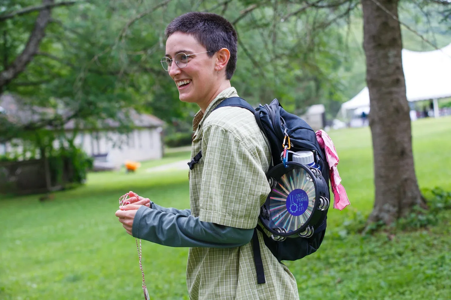 A photo of Maya smiling at the summer retreat, wearing a backpack with an attached tambourine