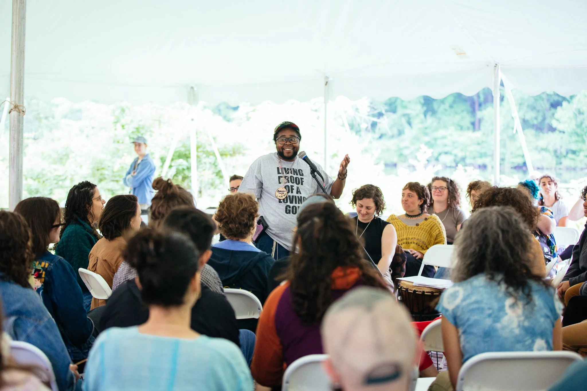 Someone stands in front of a crowd at a microphone, as the crowd sits and looks on