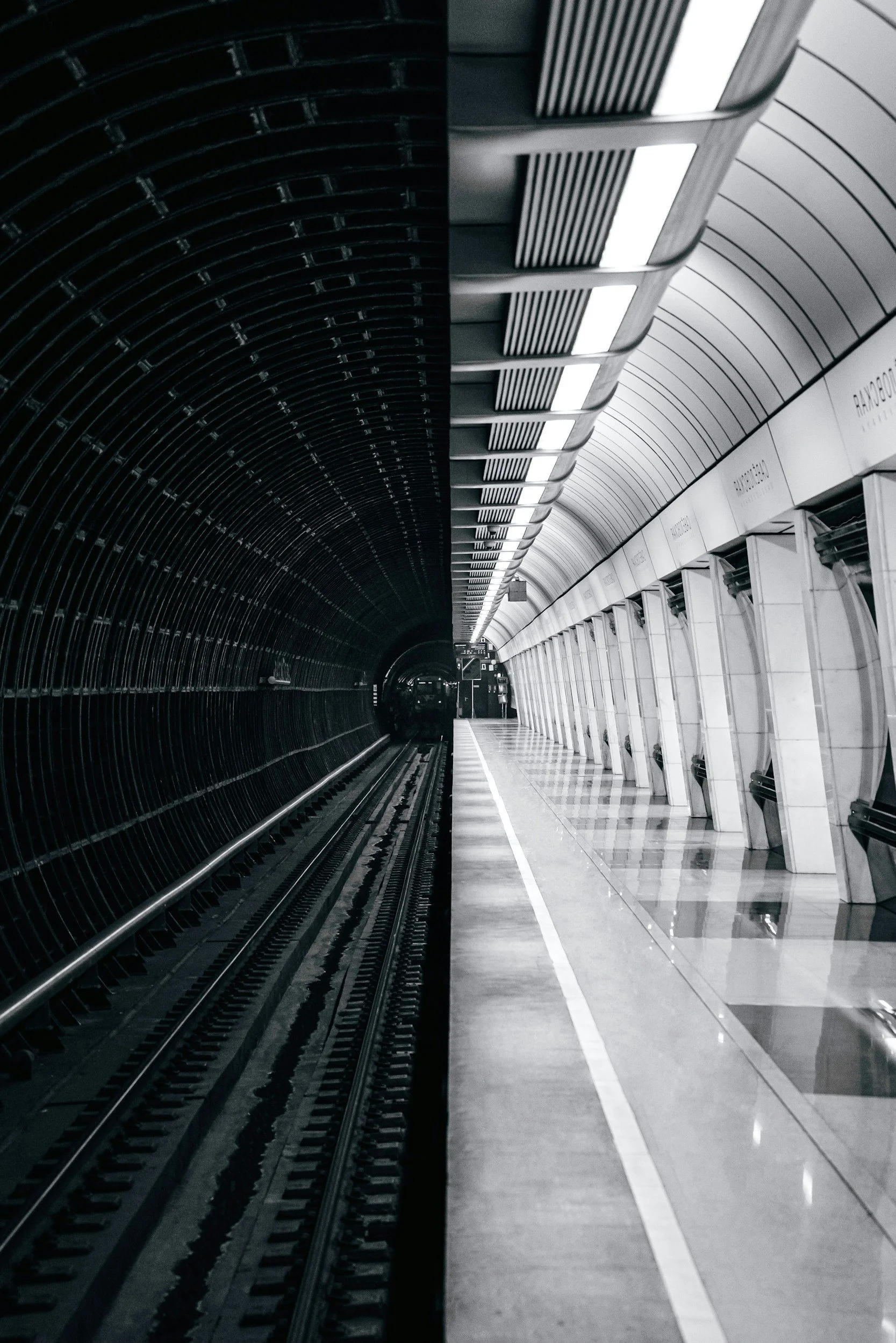 Empty metro train station platform with train tracks on the left and a lined-up row of ticket vending machines on the right, with a curved ceiling overhead.
