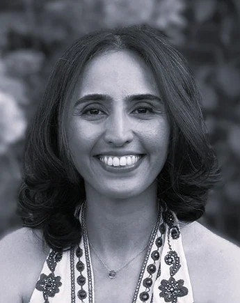 Black and white photo of a smiling woman with shoulder-length hair, wearing a patterned top and a necklace.