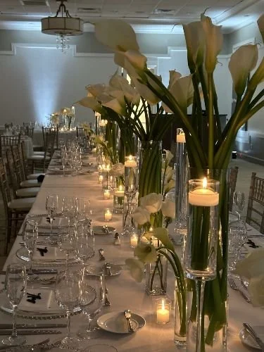 Elegant dining table decorated with tall floral arrangements, candles, and glassware in a sophisticated setting.