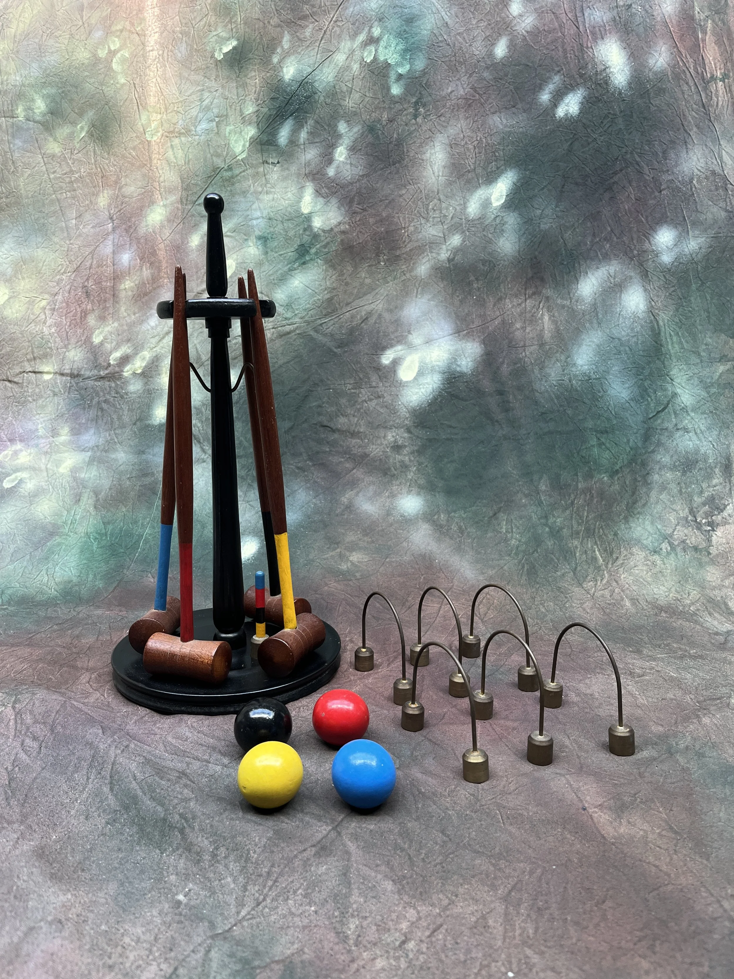 A collection of game pieces including colored balls, a small mallet, and metal hooks on a textured surface with a colorful abstract background.