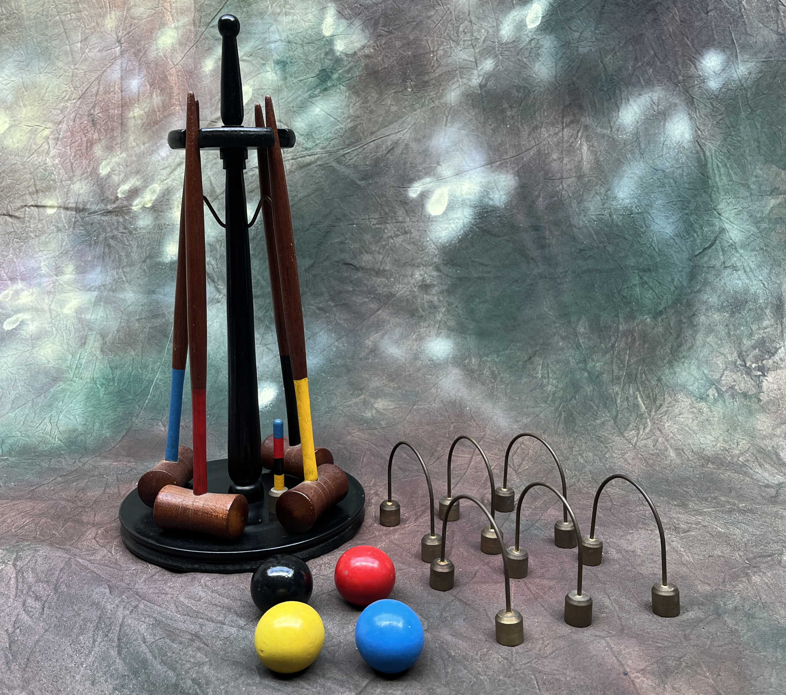 Various croquet equipment, including mallets with wooden handles and rubber or plastic heads, as well as colorful balls and metal hoops, arranged on a textured surface for a game of croquet.
