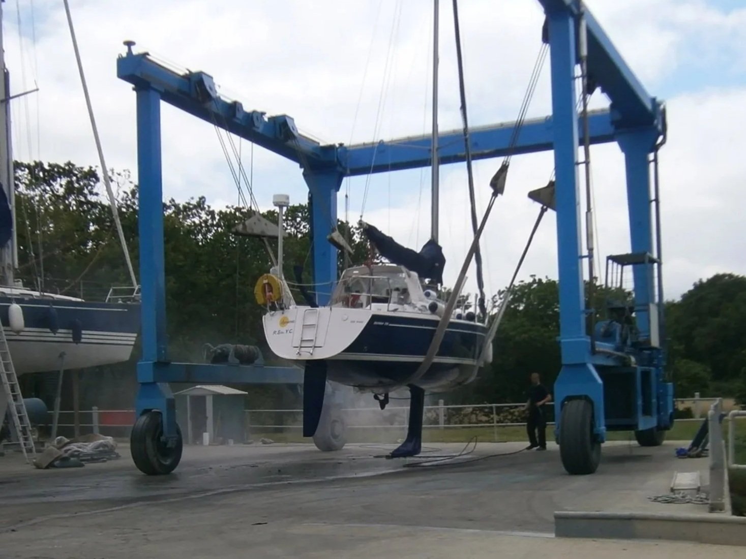 Boat hoisted out of the water on a large blue boat lift at a marina with trees in the background.