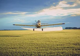 An airplane landing on a grassy field with a cloudy sky in the background.