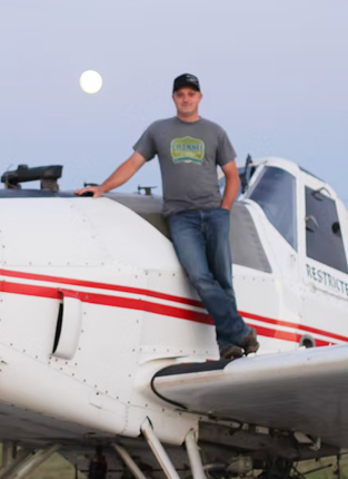 Man standing on the wing of a white aircraft outdoors during dusk, with the moon visible in the sky.