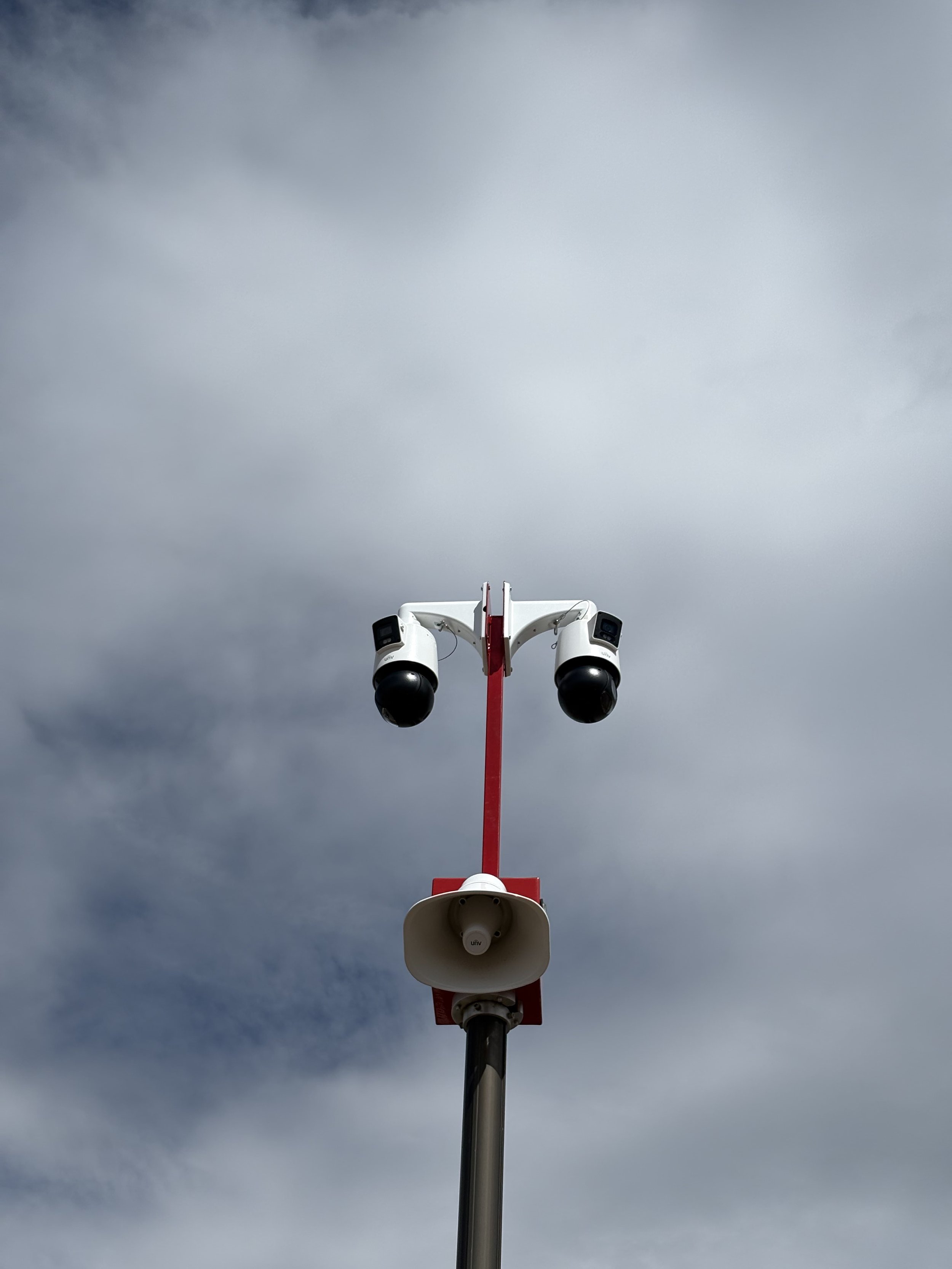 A tall pole with multiple surveillance cameras and a megaphone mounted on it, set against a cloudy sky.