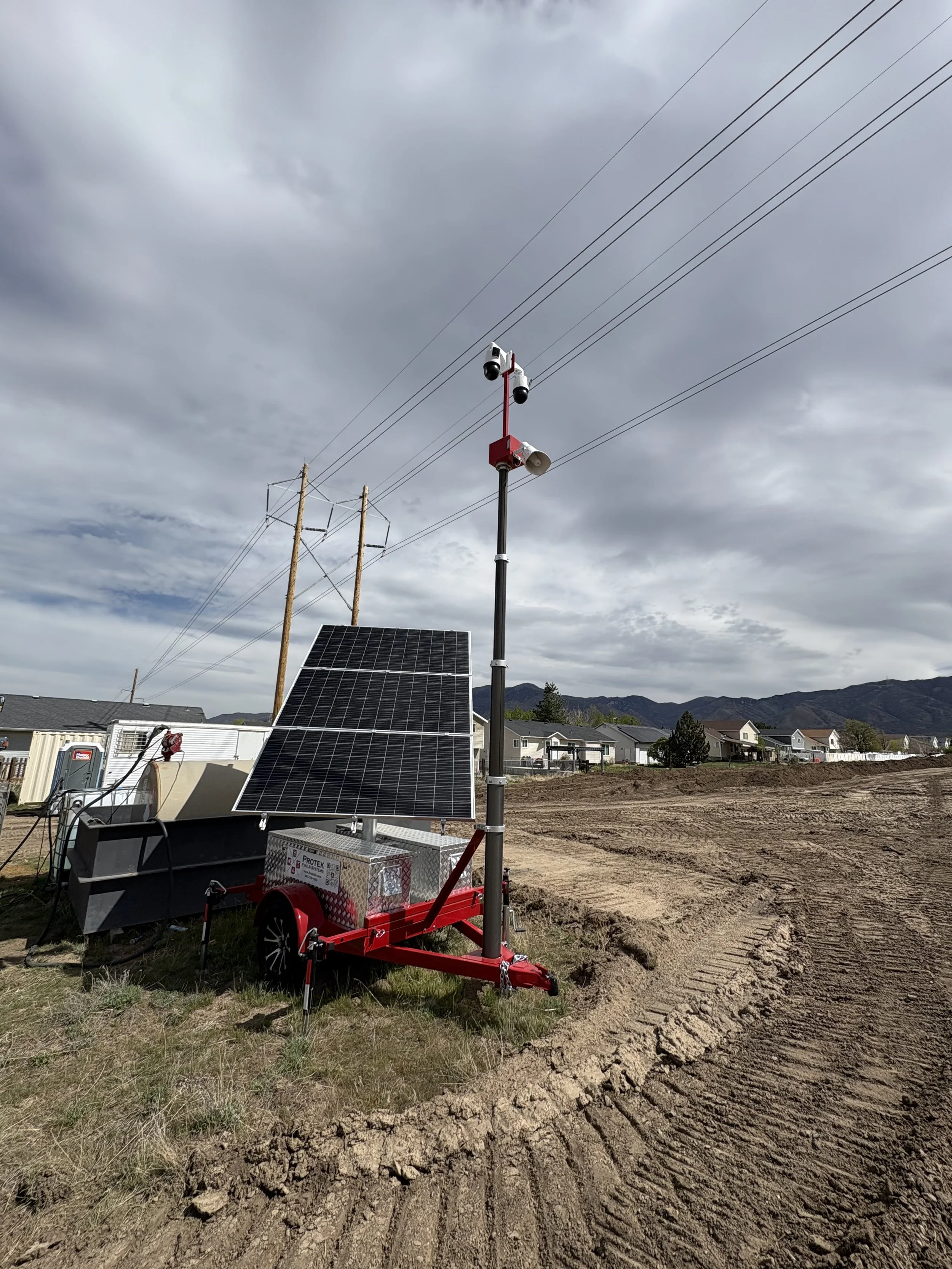A solar panel and a weather station with cameras on a trailer in a residential area with mountains in the background.