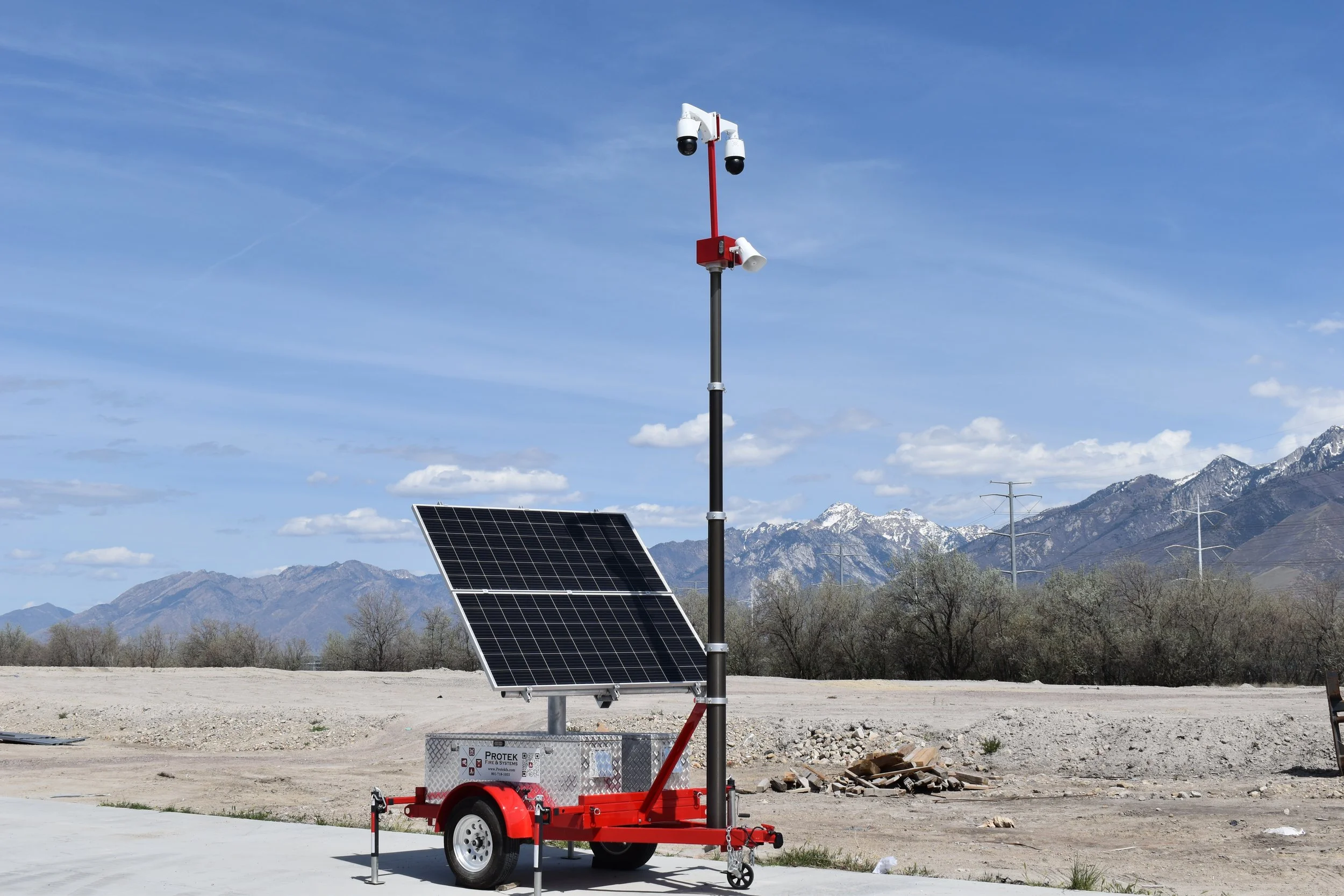 Portable solar-powered weather station with cameras on a pole and a solar panel, set against mountains and blue sky.