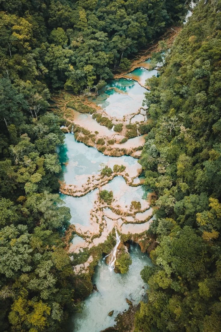 Aerial view of tiered turquoise waterfalls flowing through a lush green forest.