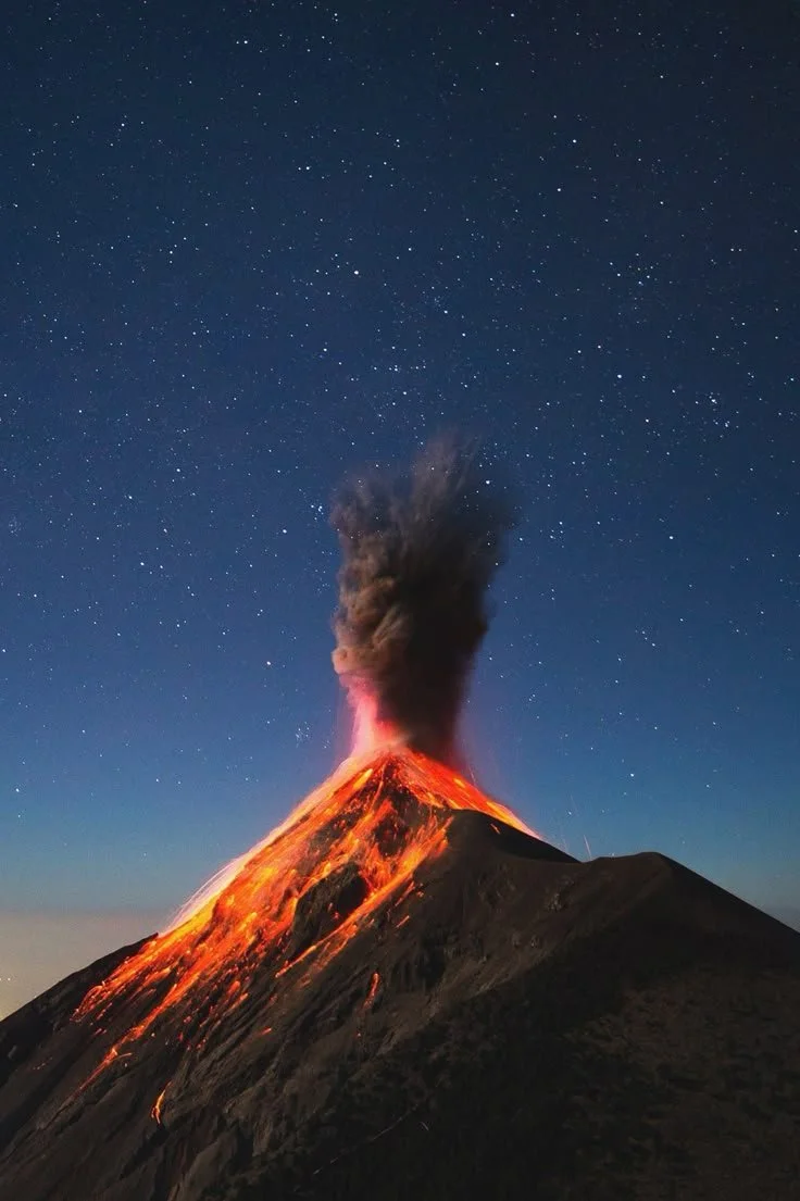 Erupting volcano spewing lava and ash into the night sky with stars overhead.