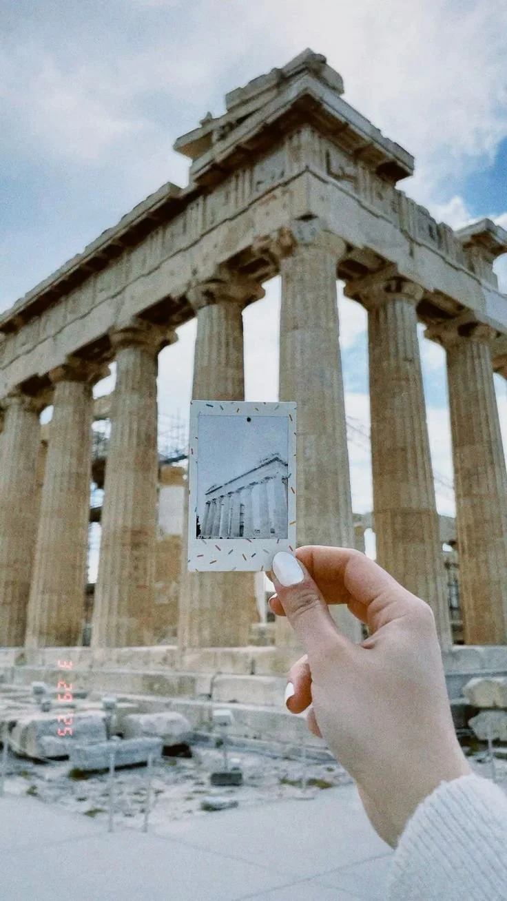 A person holding a polaroid photo of the Parthenon in front of the actual ancient Greek temple in Athens, Greece.