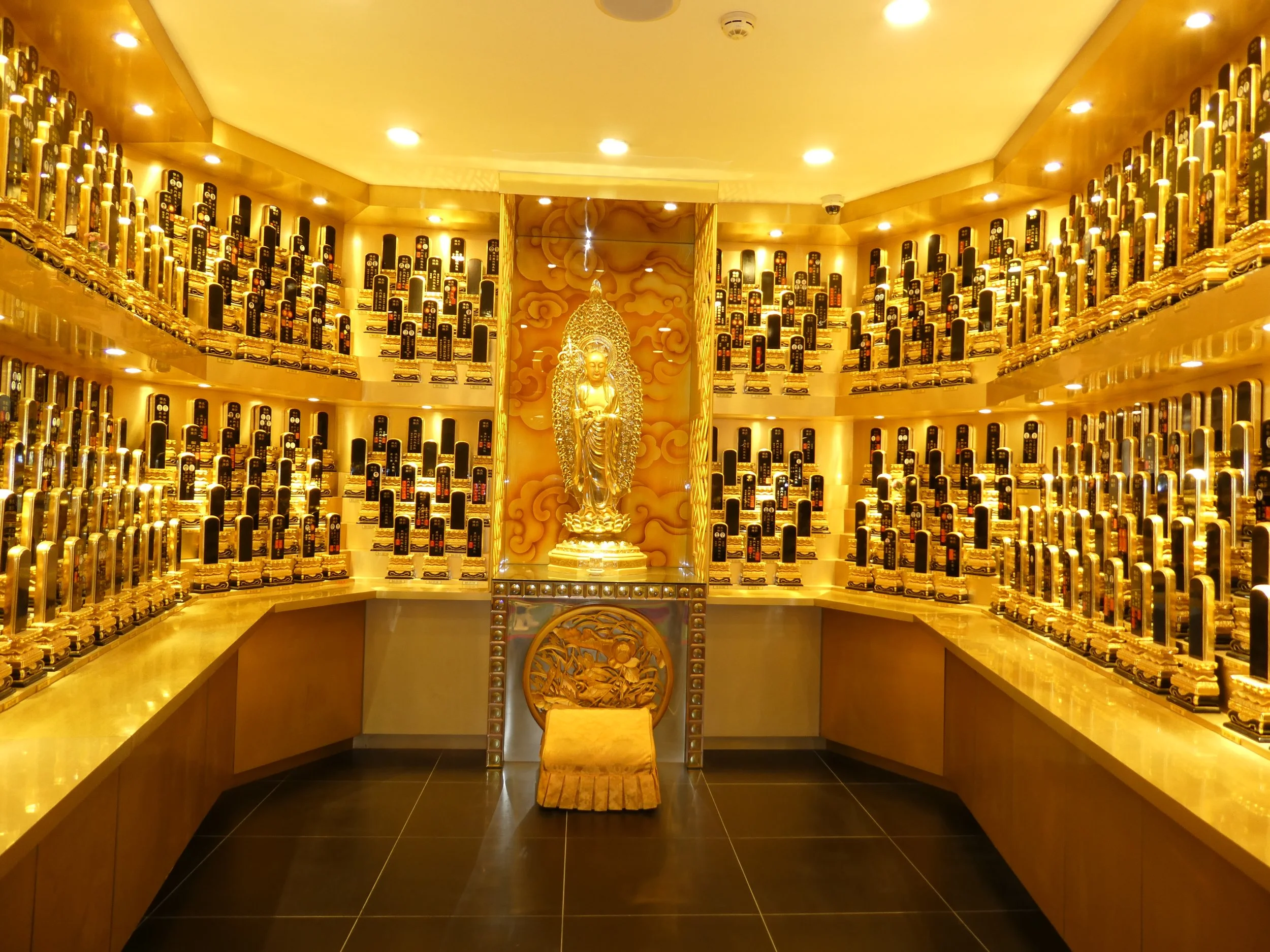A golden altar with a statue of a deity surrounded by numerous small plaques, set against a backdrop of decorative clouds.