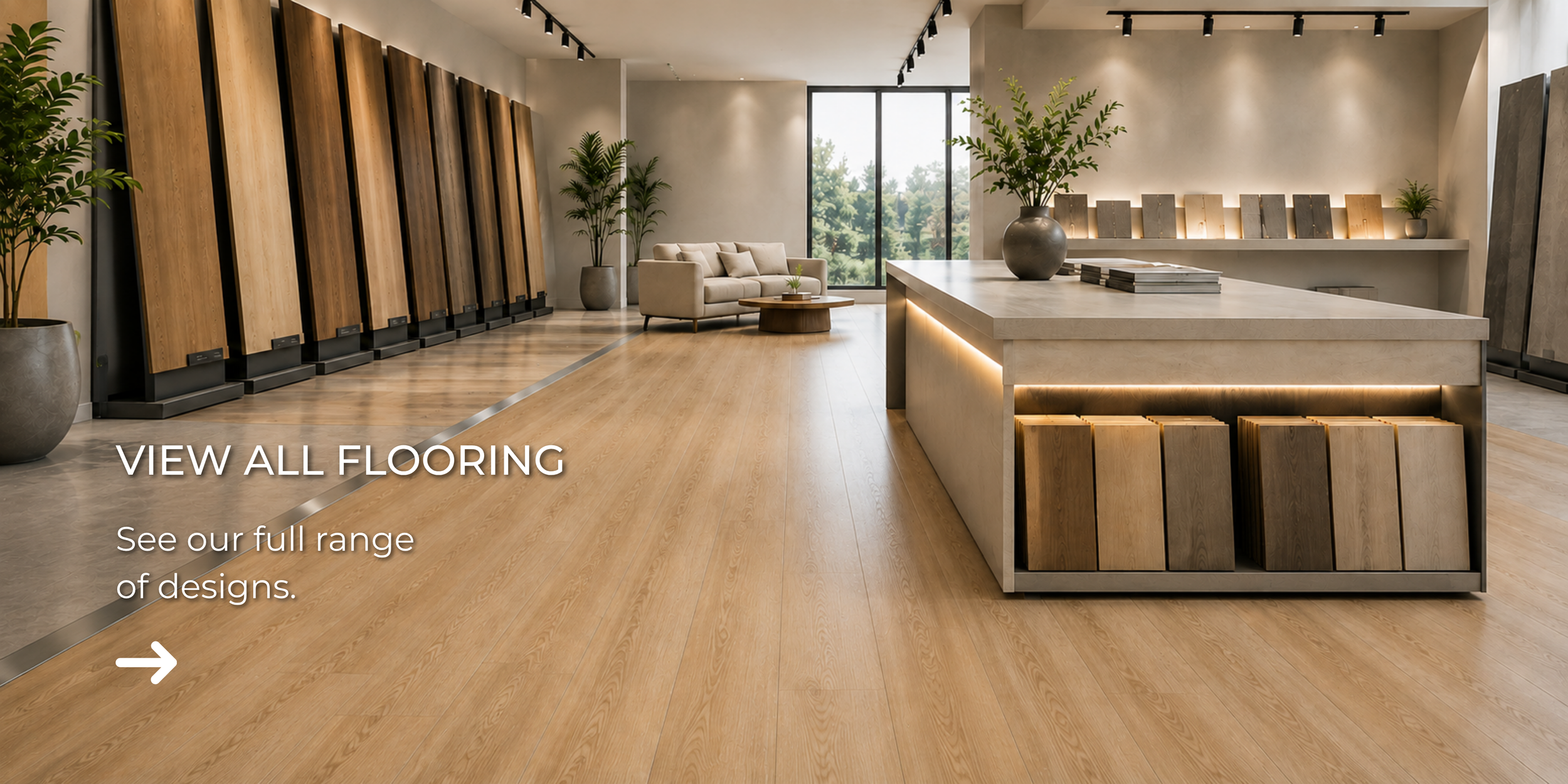 Modern showroom with wood flooring, display panels, a seating area with sofa, large window with nature view, and a central reception desk with a vase of greenery.